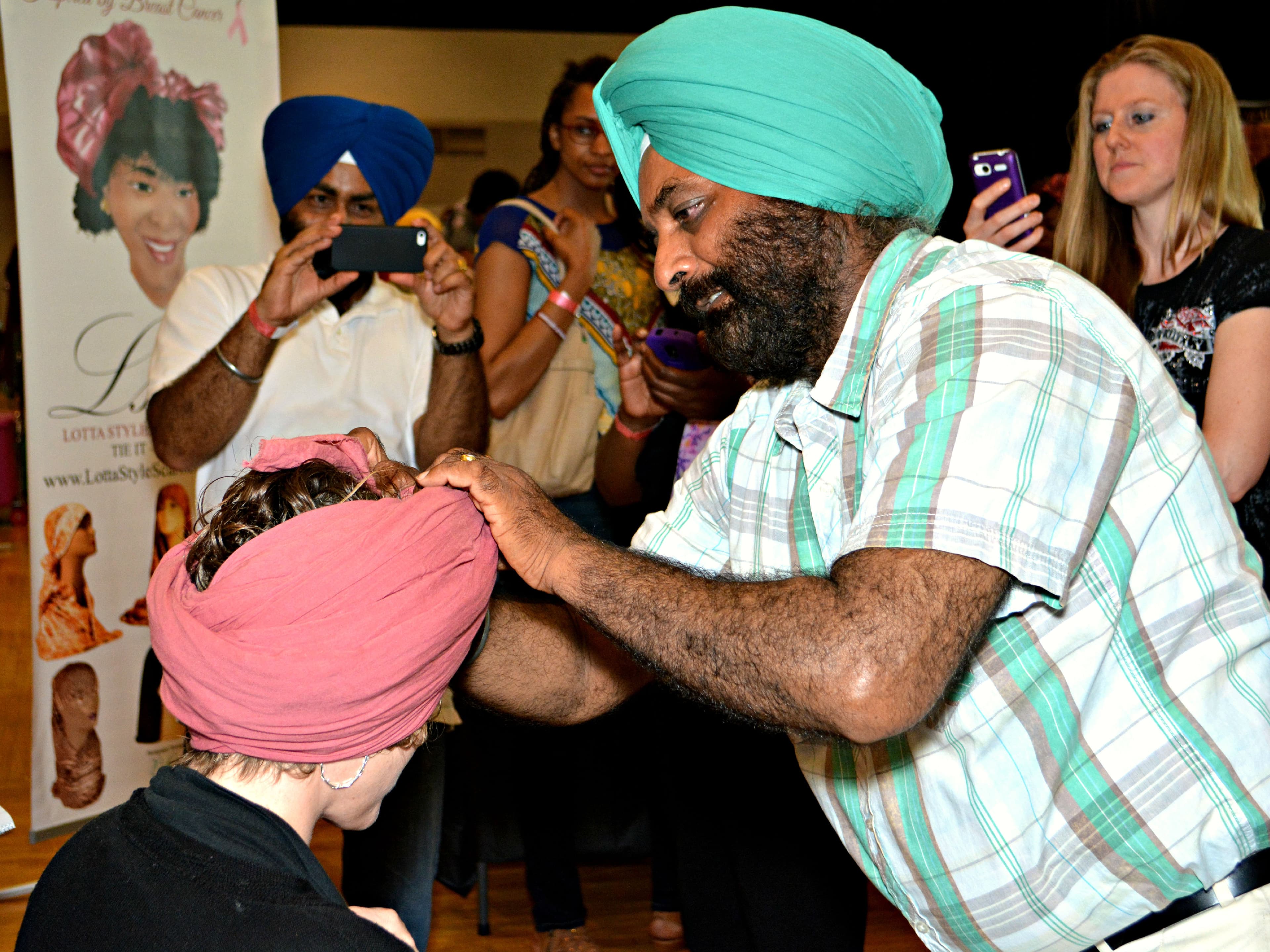 A crowd gathers around a Sikh man who is showing how to wrap a dastar or turban.