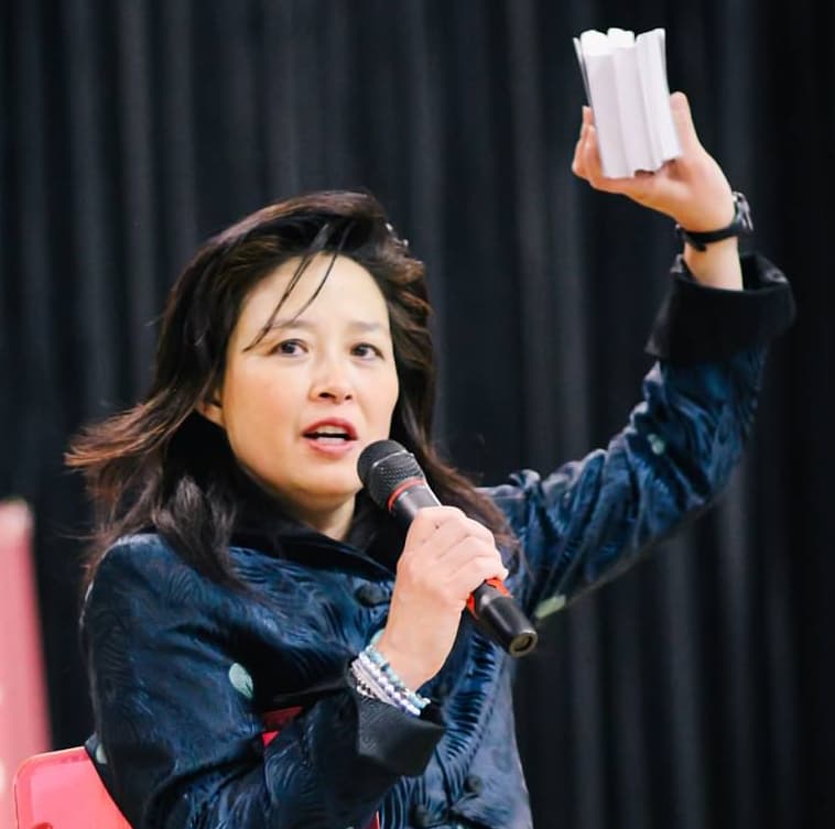A woman in a jacket is holding a microphone and talking.