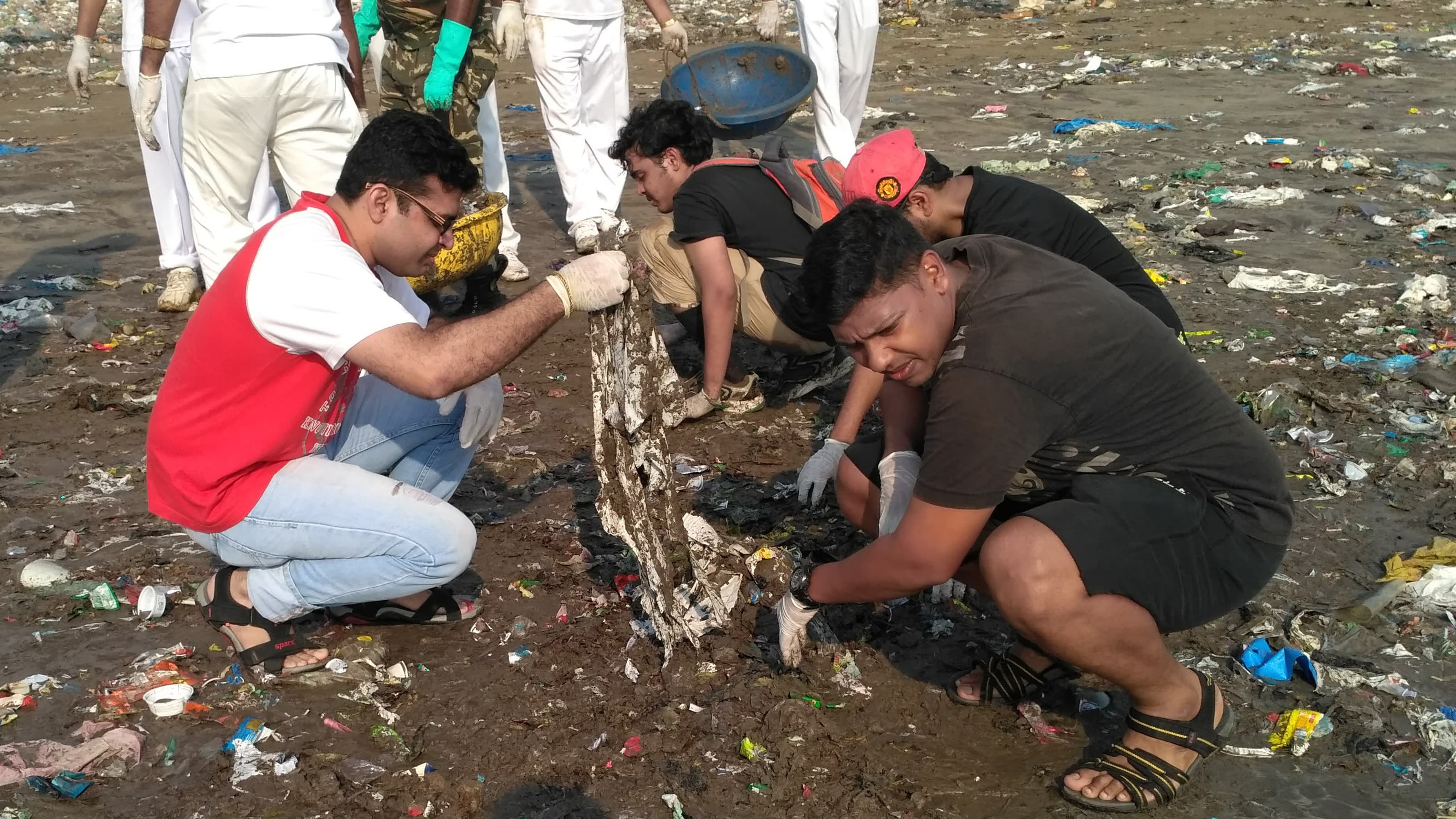 Volunteers crouch on the wet sand as they pick up trash from a beach near Mumbai's Versova jetty
