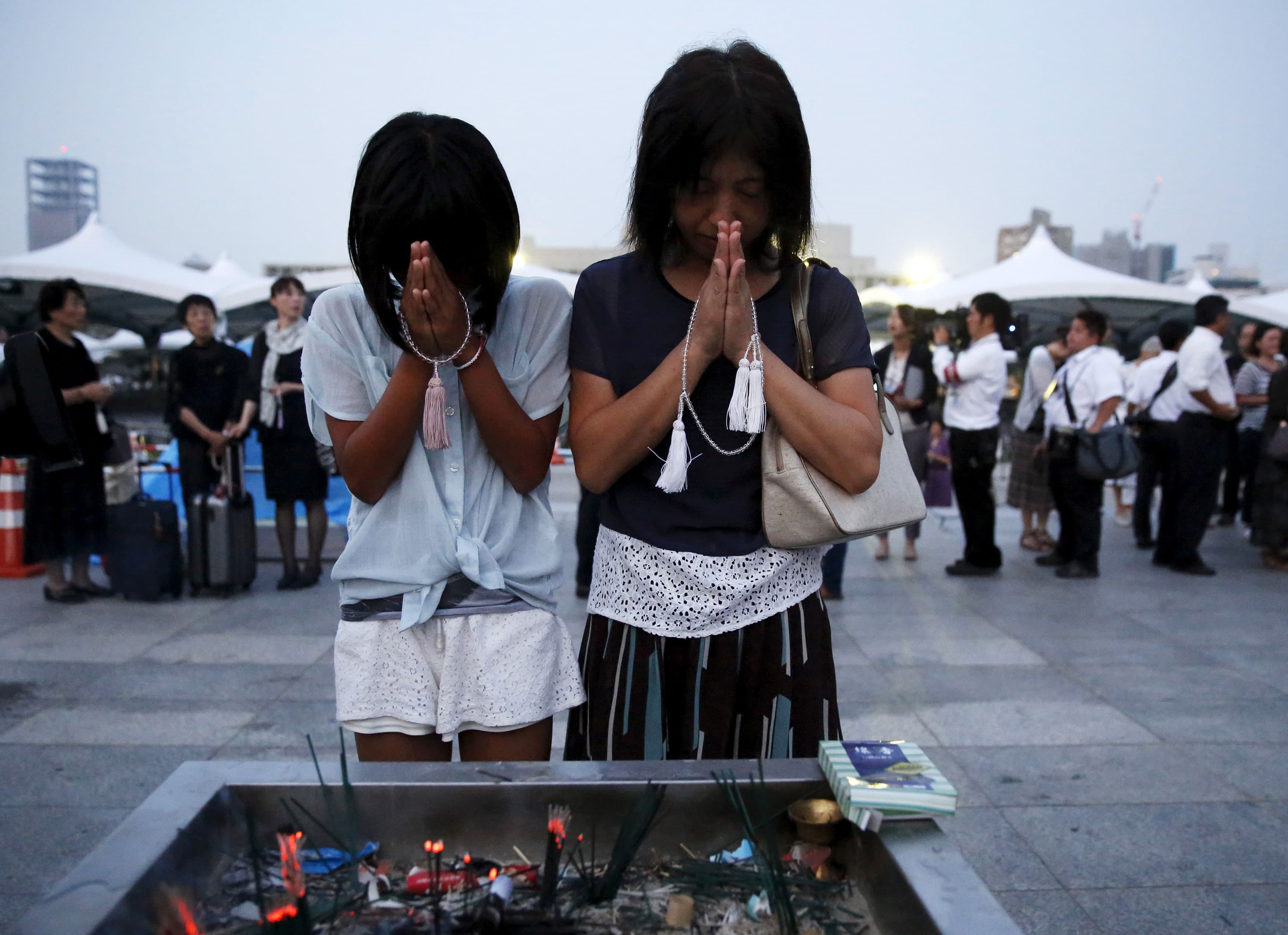 Two women play with their hands in front of their face in front of a vessel filled with burning incense sticks