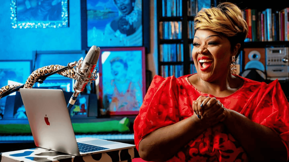 Woman in a red dress laughs and claps her hands in front of a computer screen