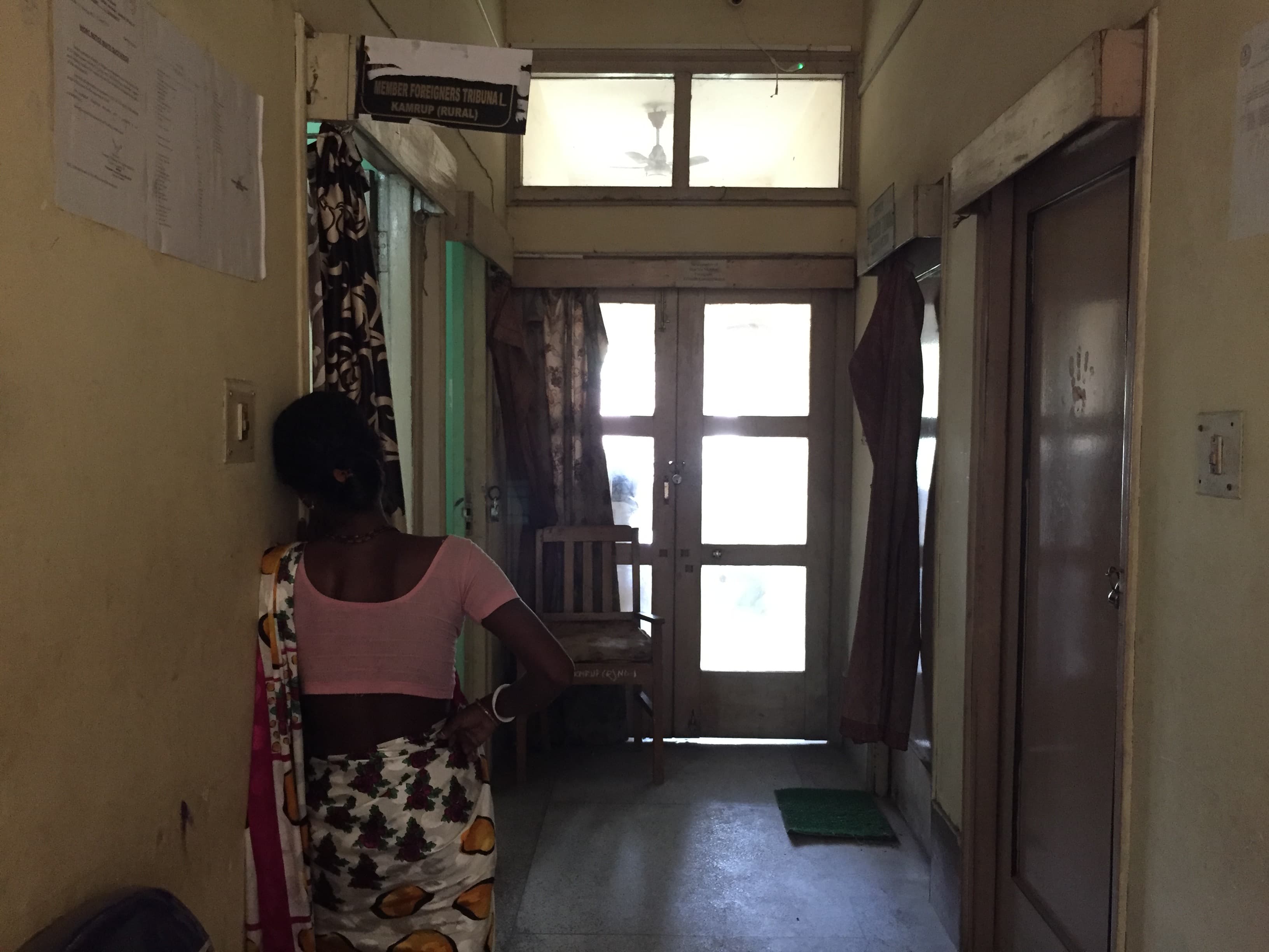 A woman wearing a pink and white saree waits in hallway