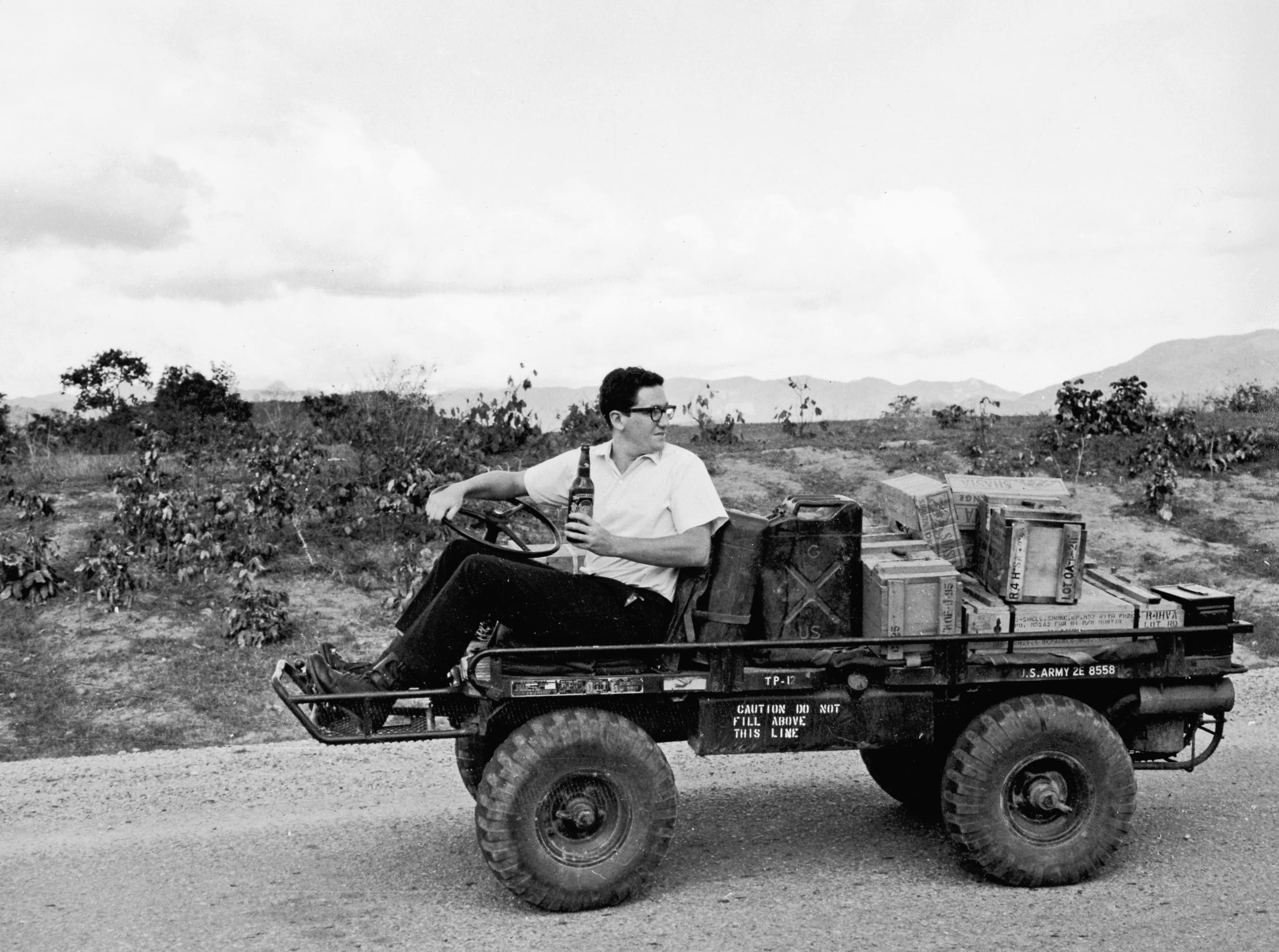 Richard Holbrooke sits in a small military vehicle holding a bottle.