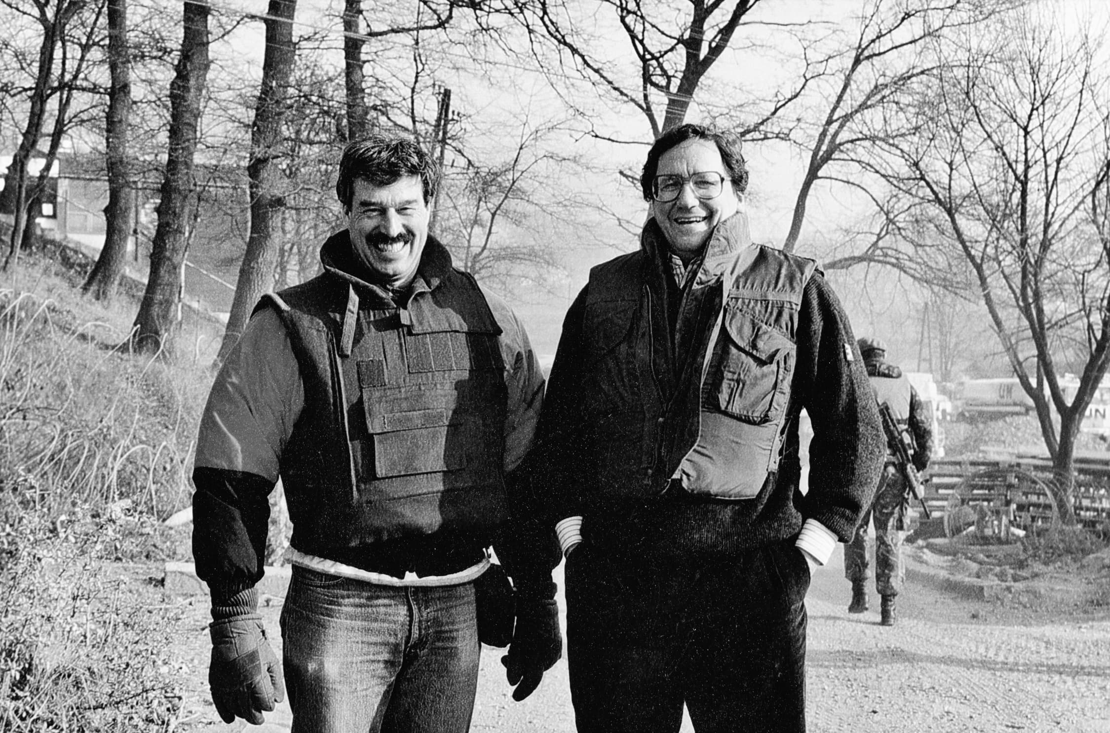Two men stand in coats on a road.