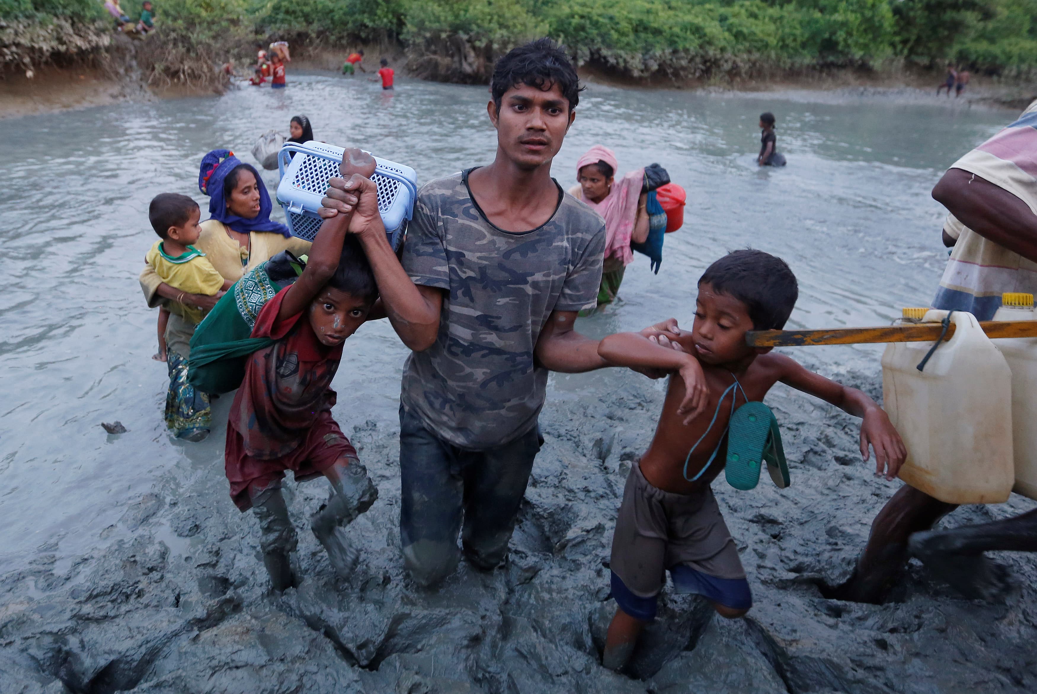 A Rohingya refugee helps children cross the mud after crossing the Naf River at the Bangladesh-Myanmar border.