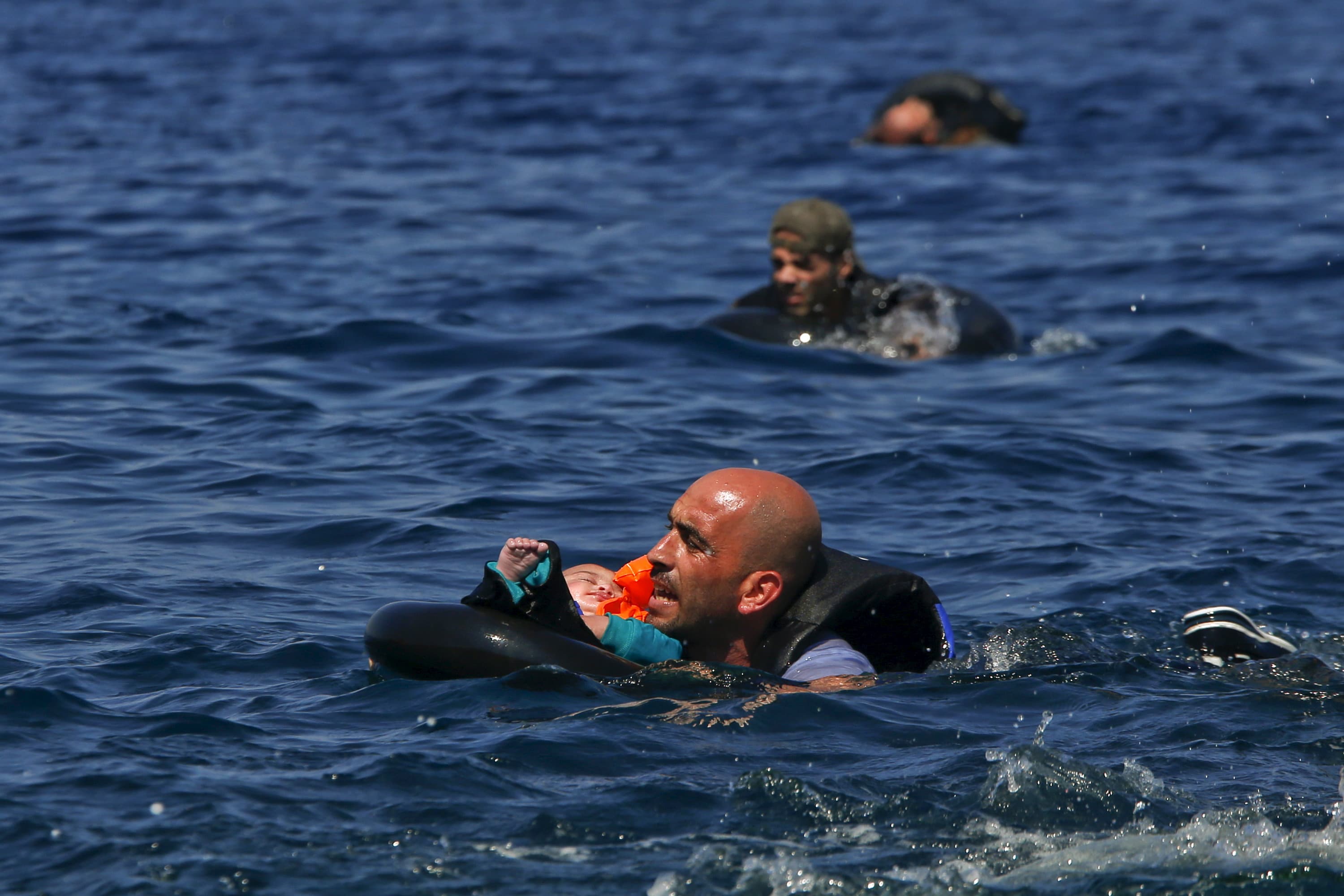 A Syrian refugee holding a baby in a life tube swims towards the shore, after their dinghy deflated some 100 yards from the Greek island of Lesbos, September 13th 2015.