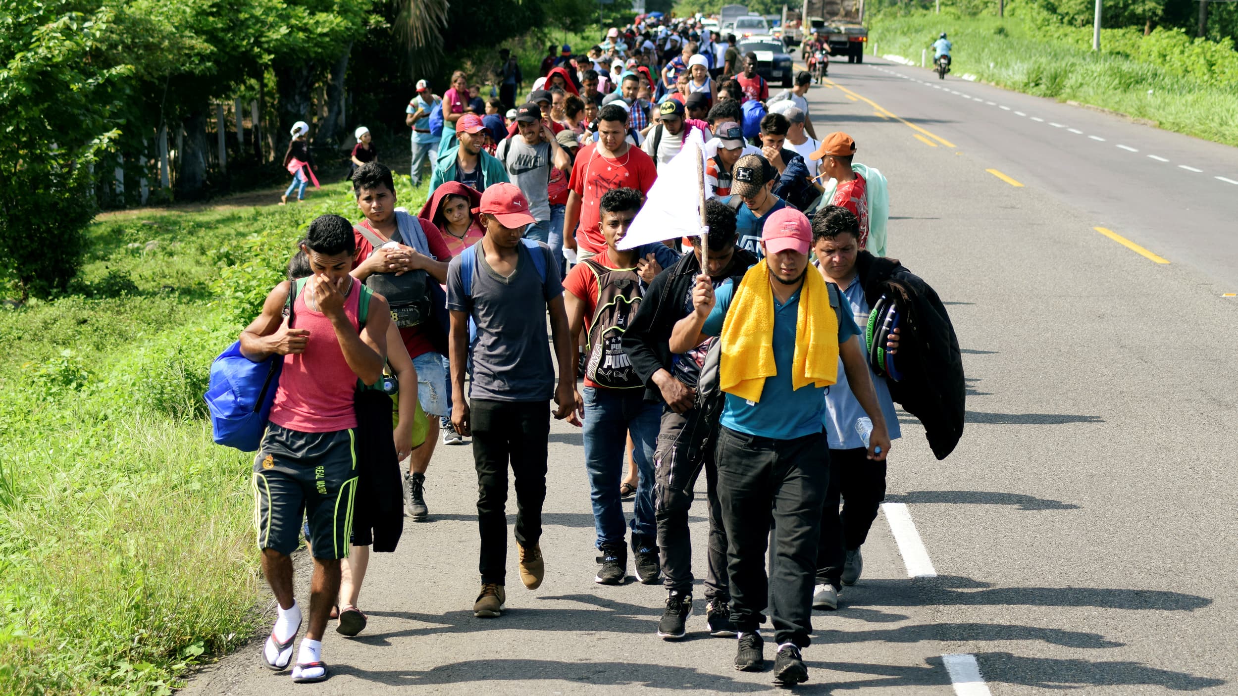 A line of migrants carries bags and walks on a road