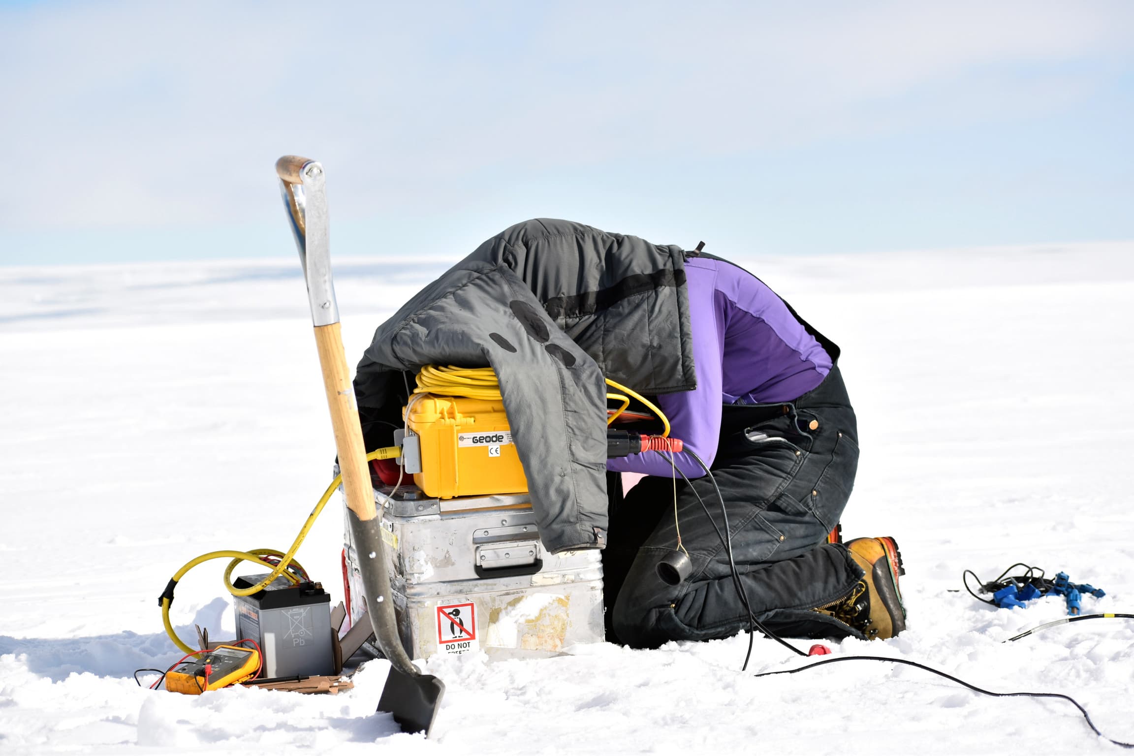 A person is kneeling on the snow with a coat over their head.