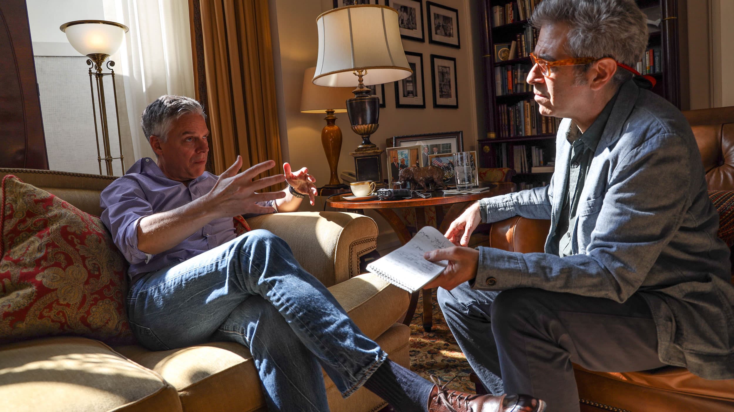 Ambassador Jon Huntsman Jr. is shown in a button down shirt sitting across from Marco Werman who is wearing glasses.