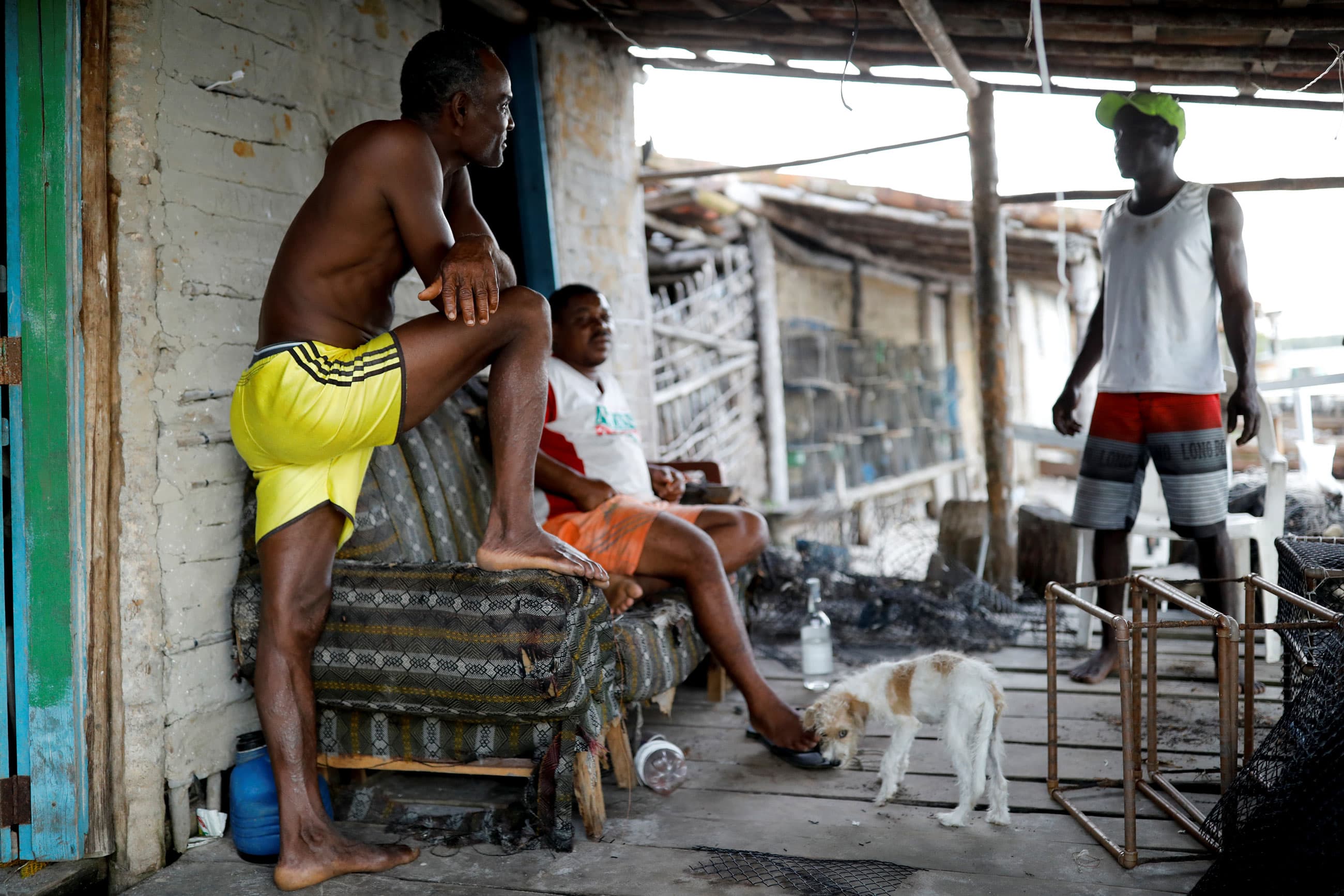 A man is shown with one leg up, leaning on furniture and talking to two other men.