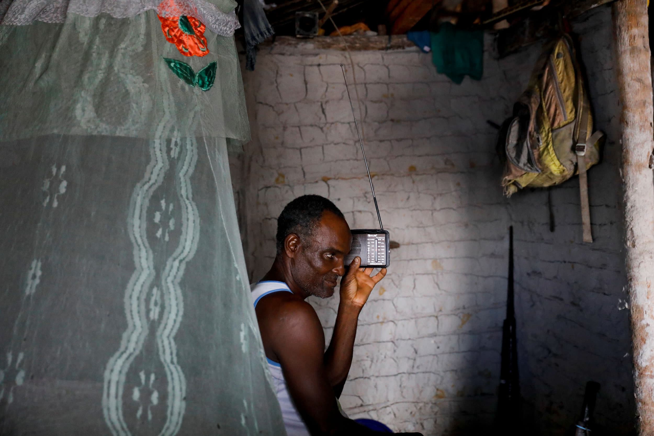 A man is shown sitting with a small radio held next to his ear.