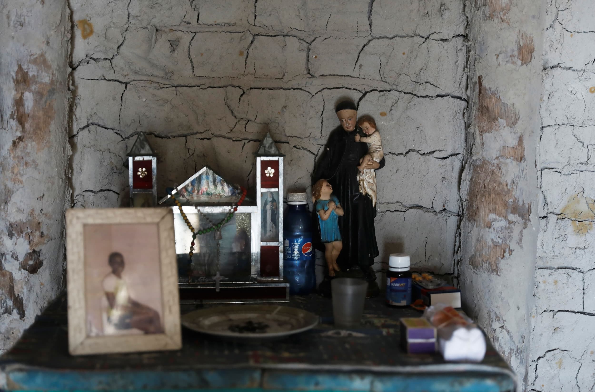 A shrine is seen with a framed photograph, a bottle of Pepsi and other items on a shelf.