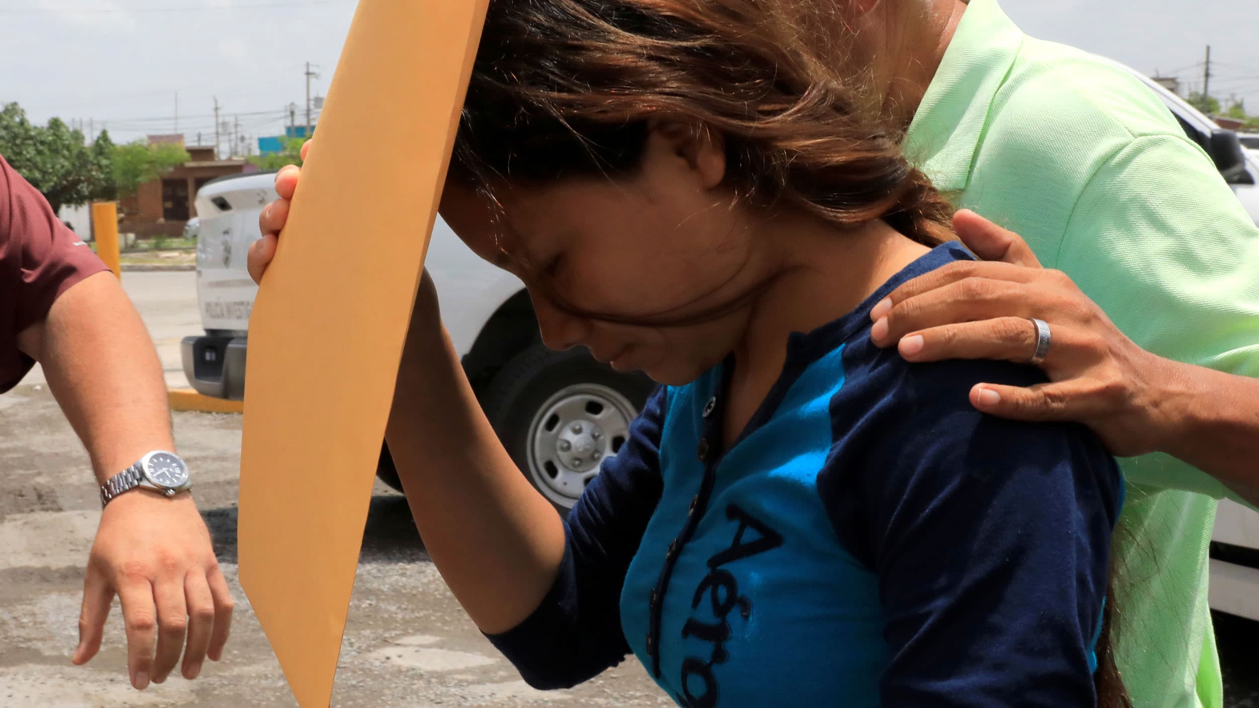 A woman with a blue shirt on is walking past the camera with a large envelop in her hand covering her face.