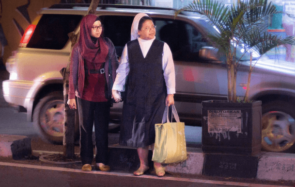 A Catholic and Muslim hold hands as they cross the street