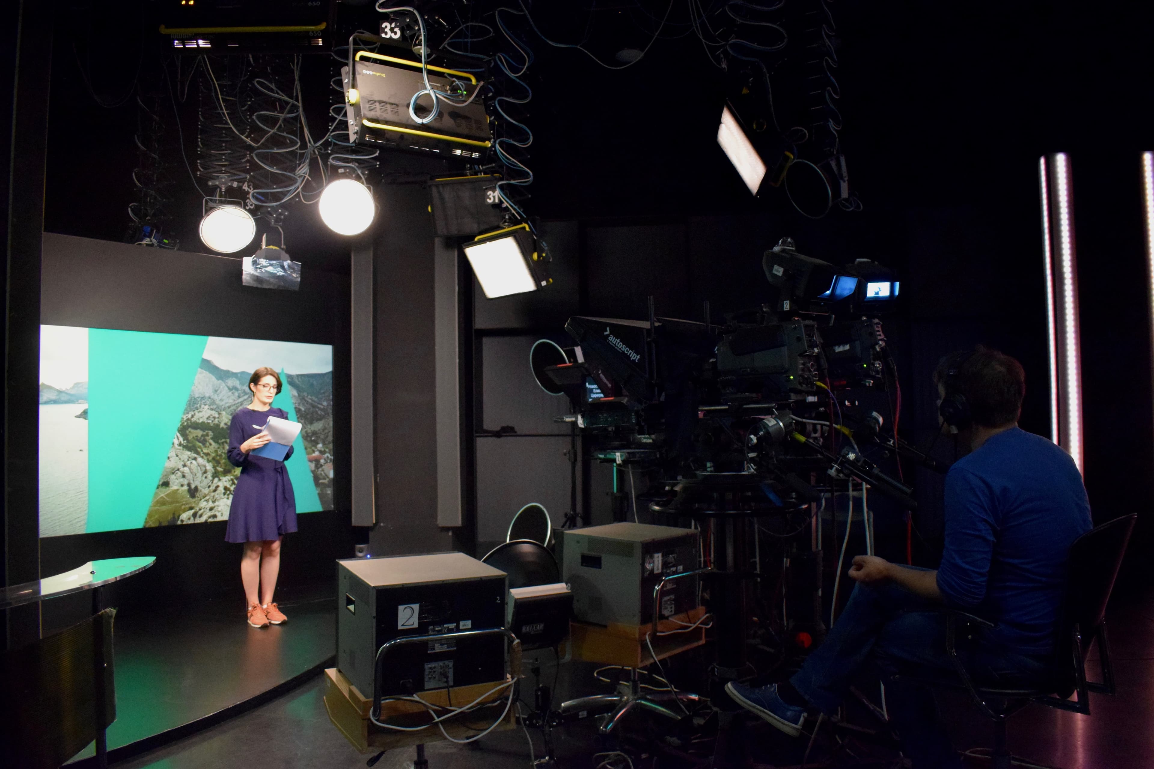 A woman wears blue dress and gym shoes while presenting news in front of cameras