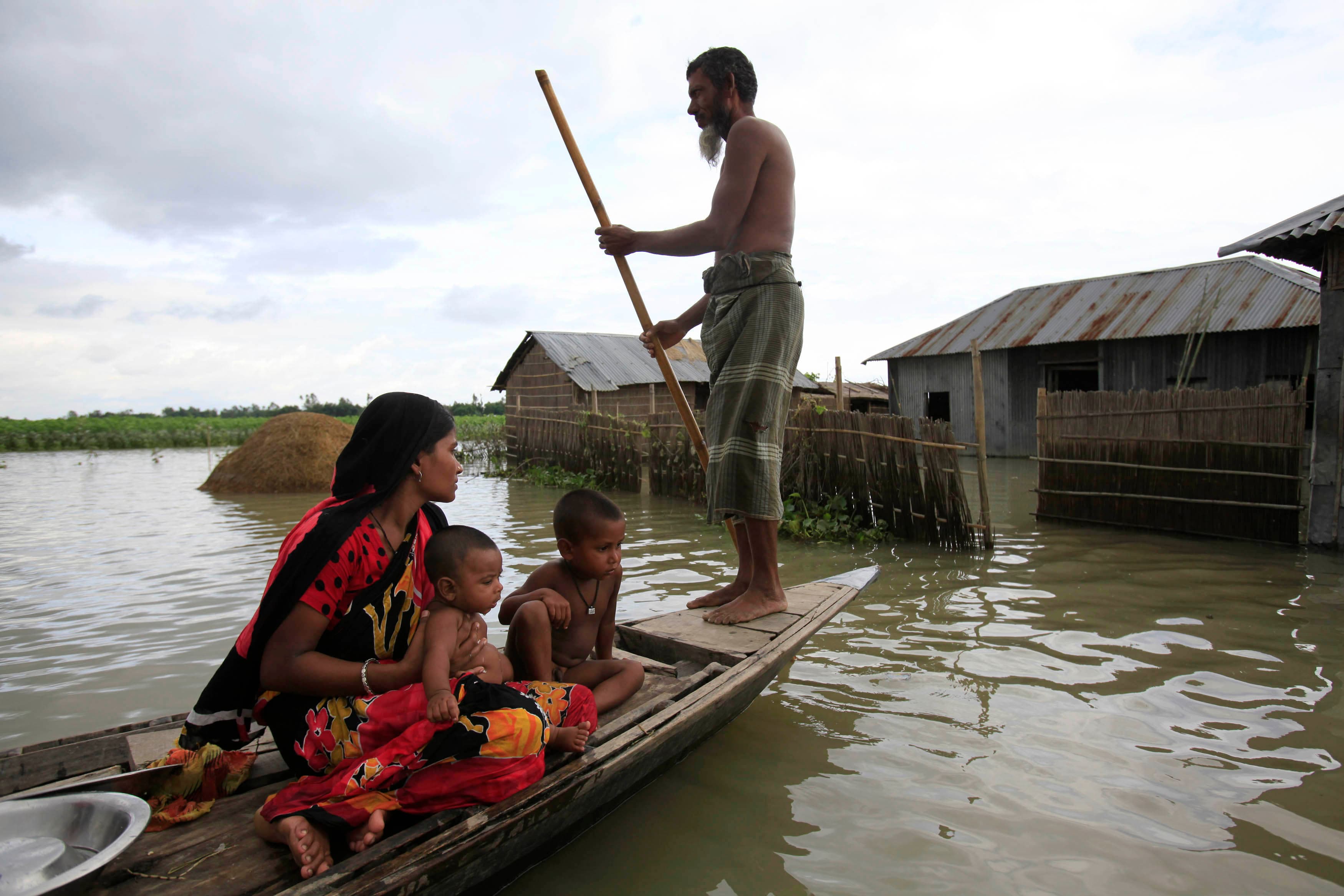 A family sits on a small boat in a flooded village.