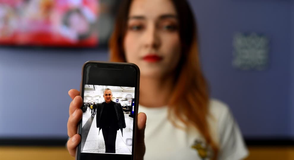 A woman holds up a picture of her father on a cellphone.