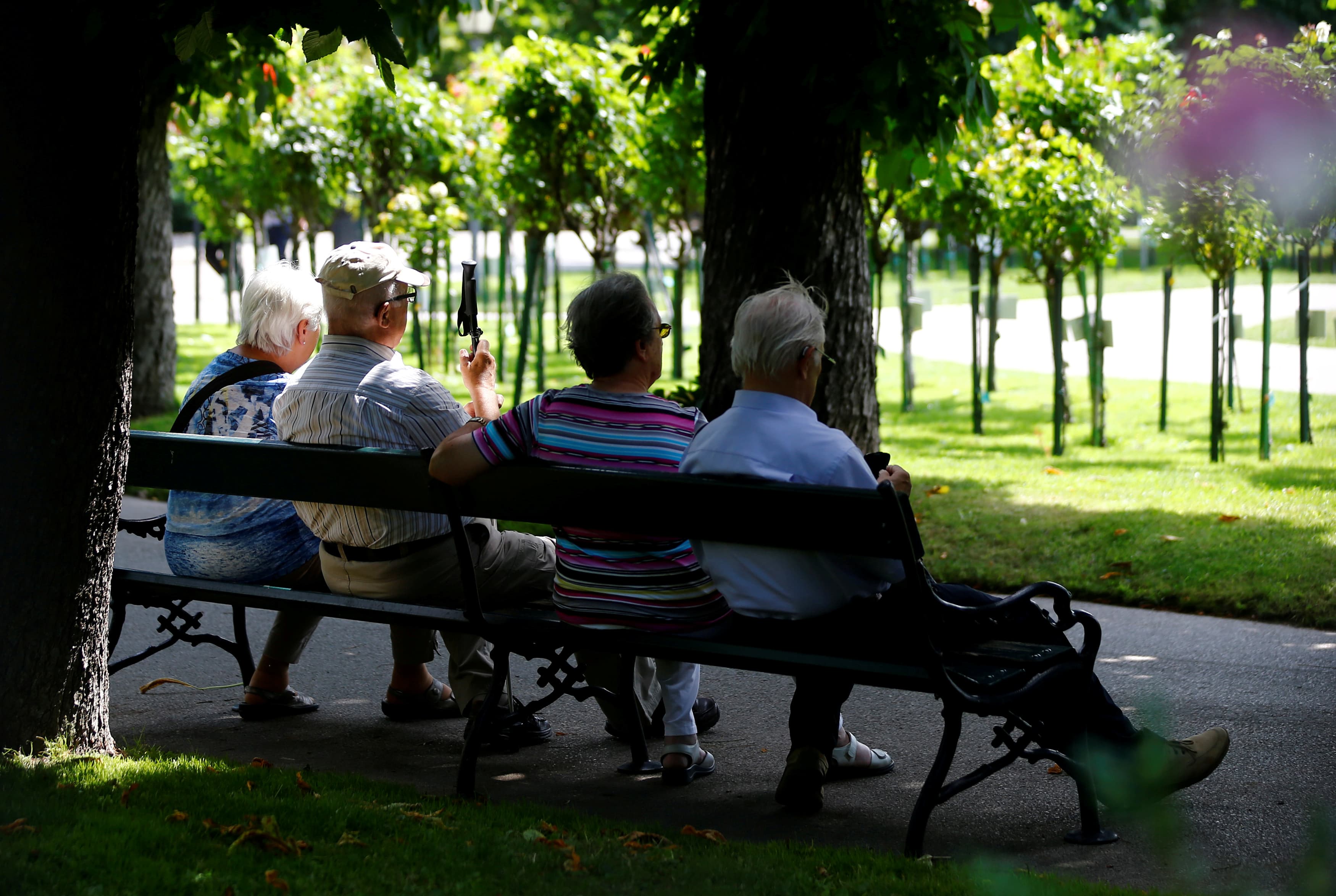 Four elderly people sit on a park bench.
