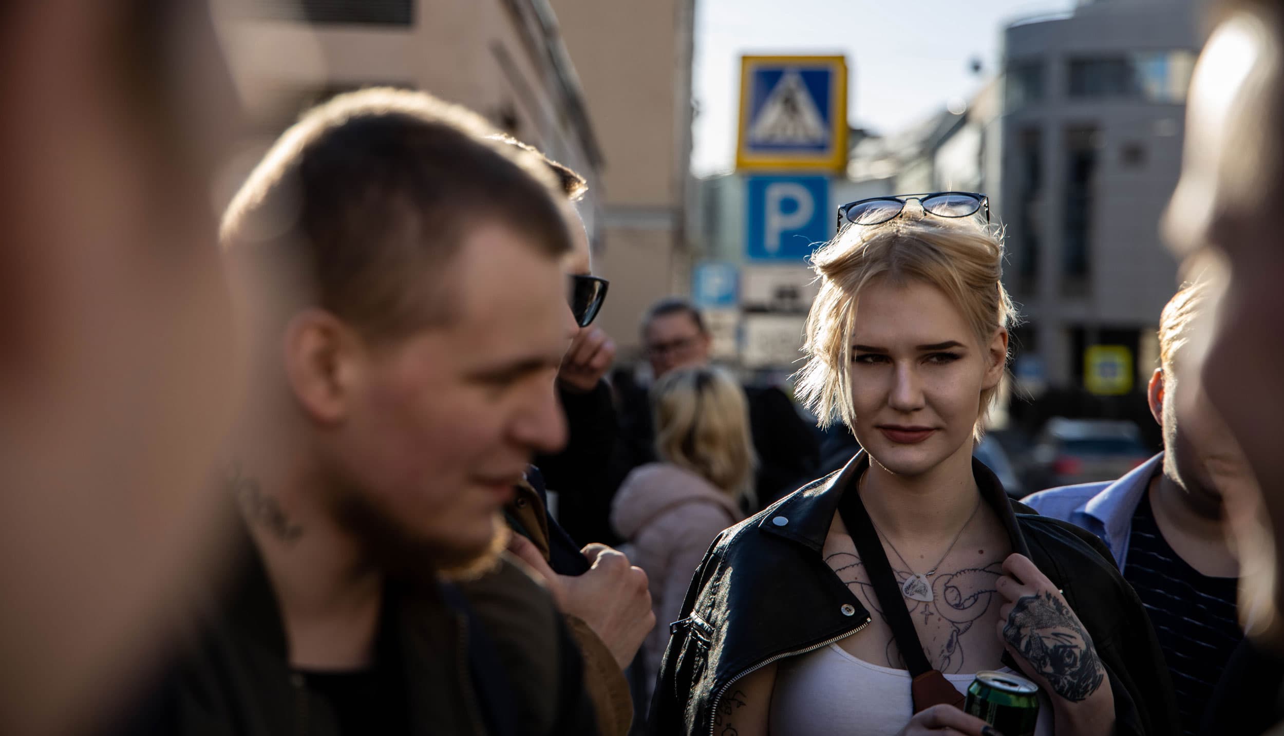 A woman with tattoos stands in a crowd outside a club.
