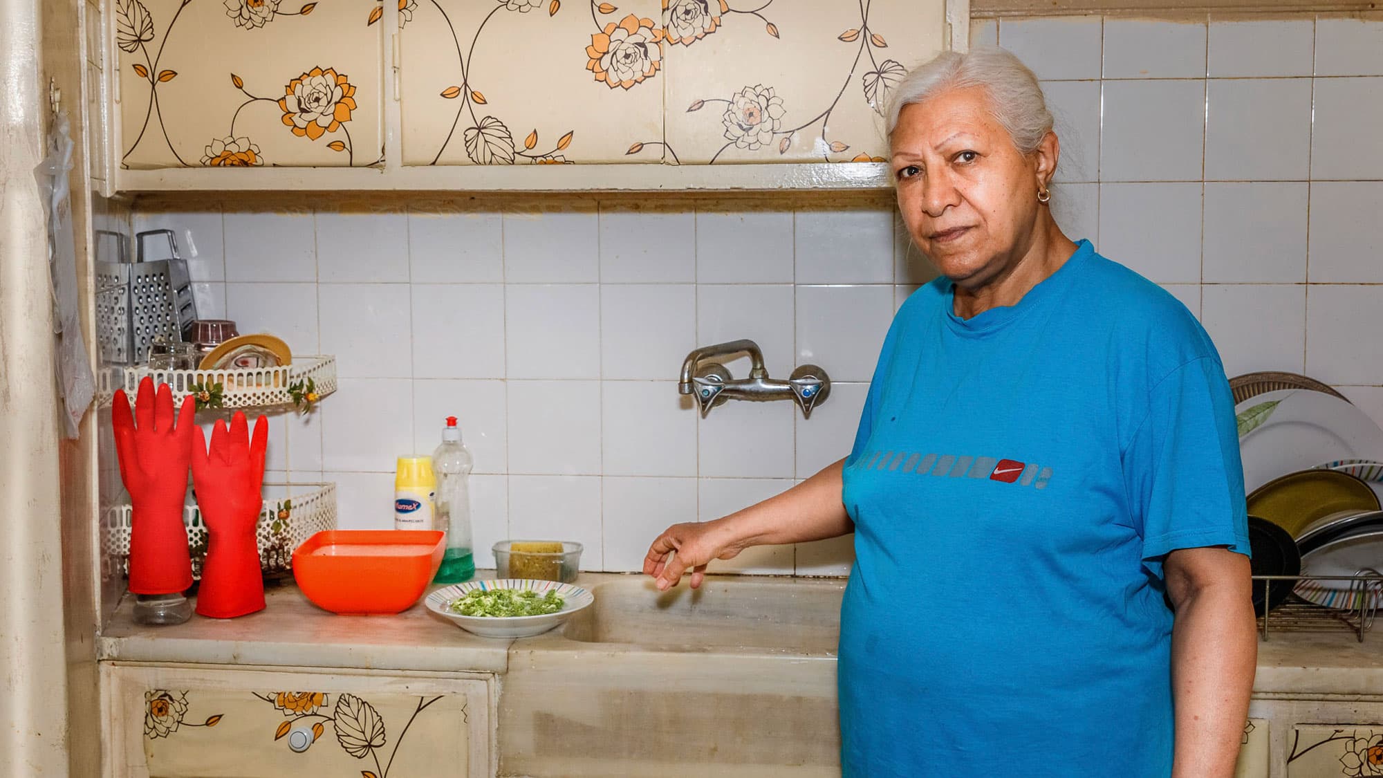 Fatemeh Khani Hakani is shown standing next to a sink and flower-lined cupboards.