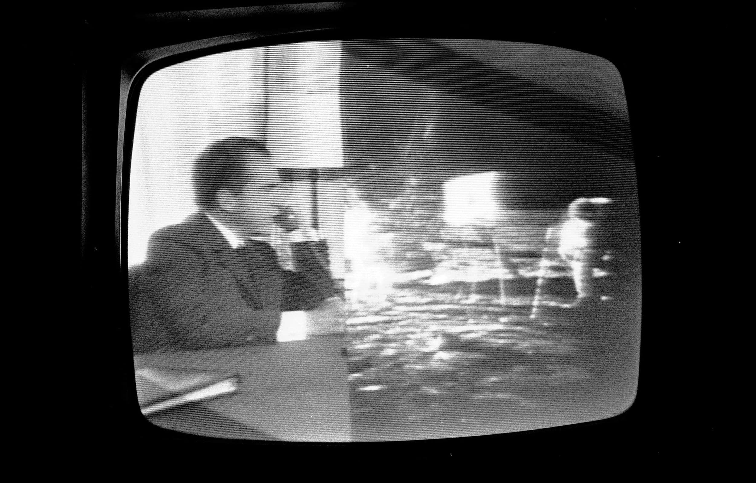 In a photograph of a television,  President Richard Nixon is shown on the left and Apollo 11 crew is shown on the right all in black and white.