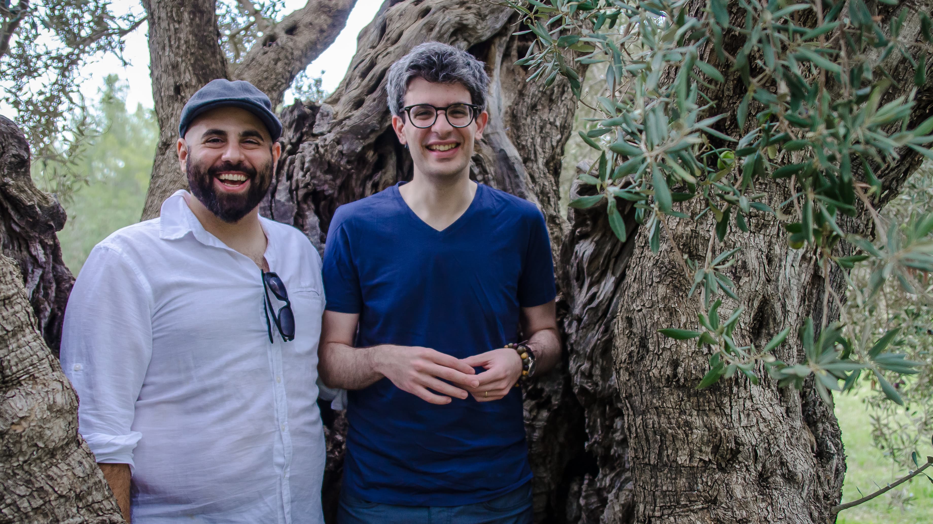 Two men pose in front of an old tree trunk.