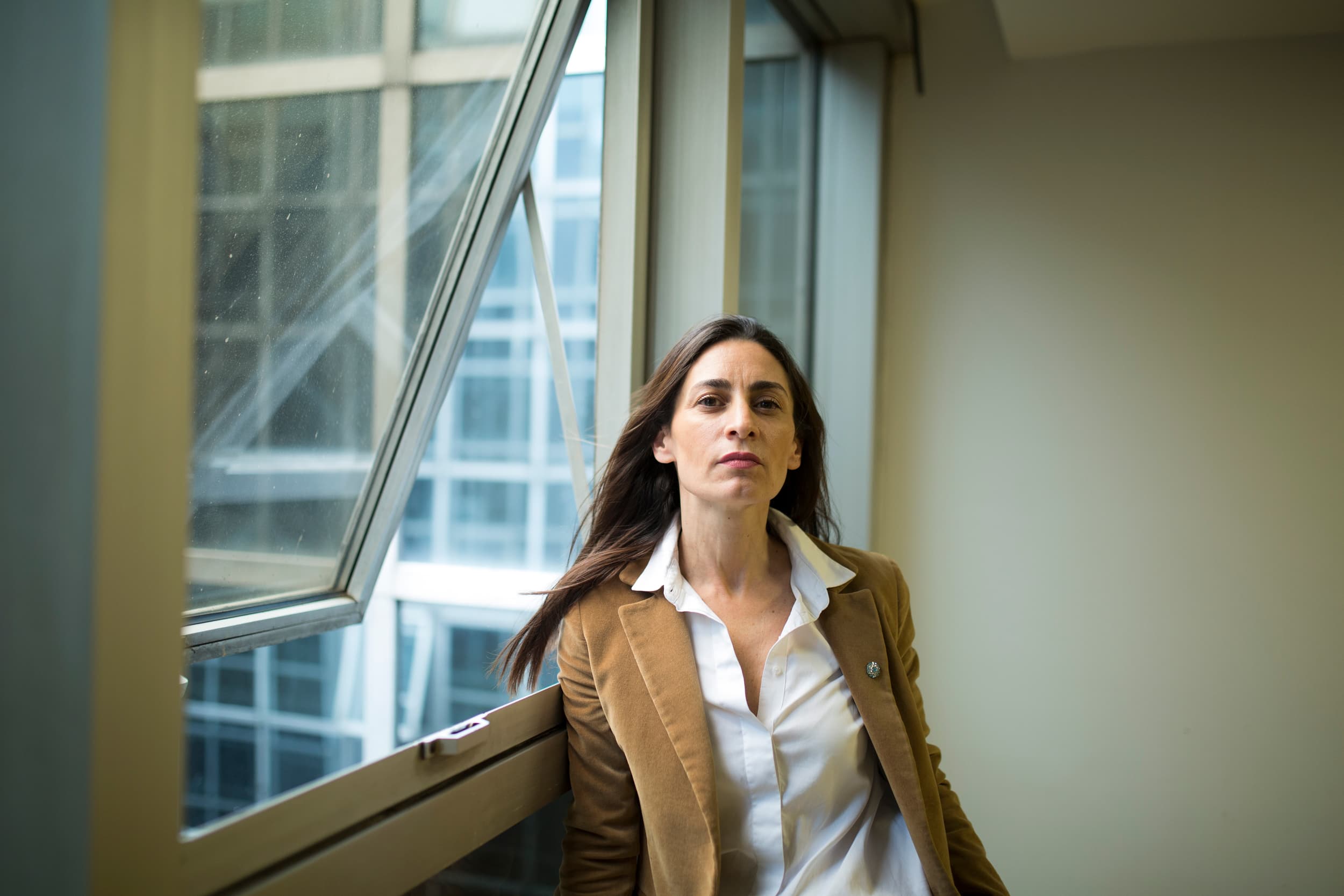 A woman stands next to a window.