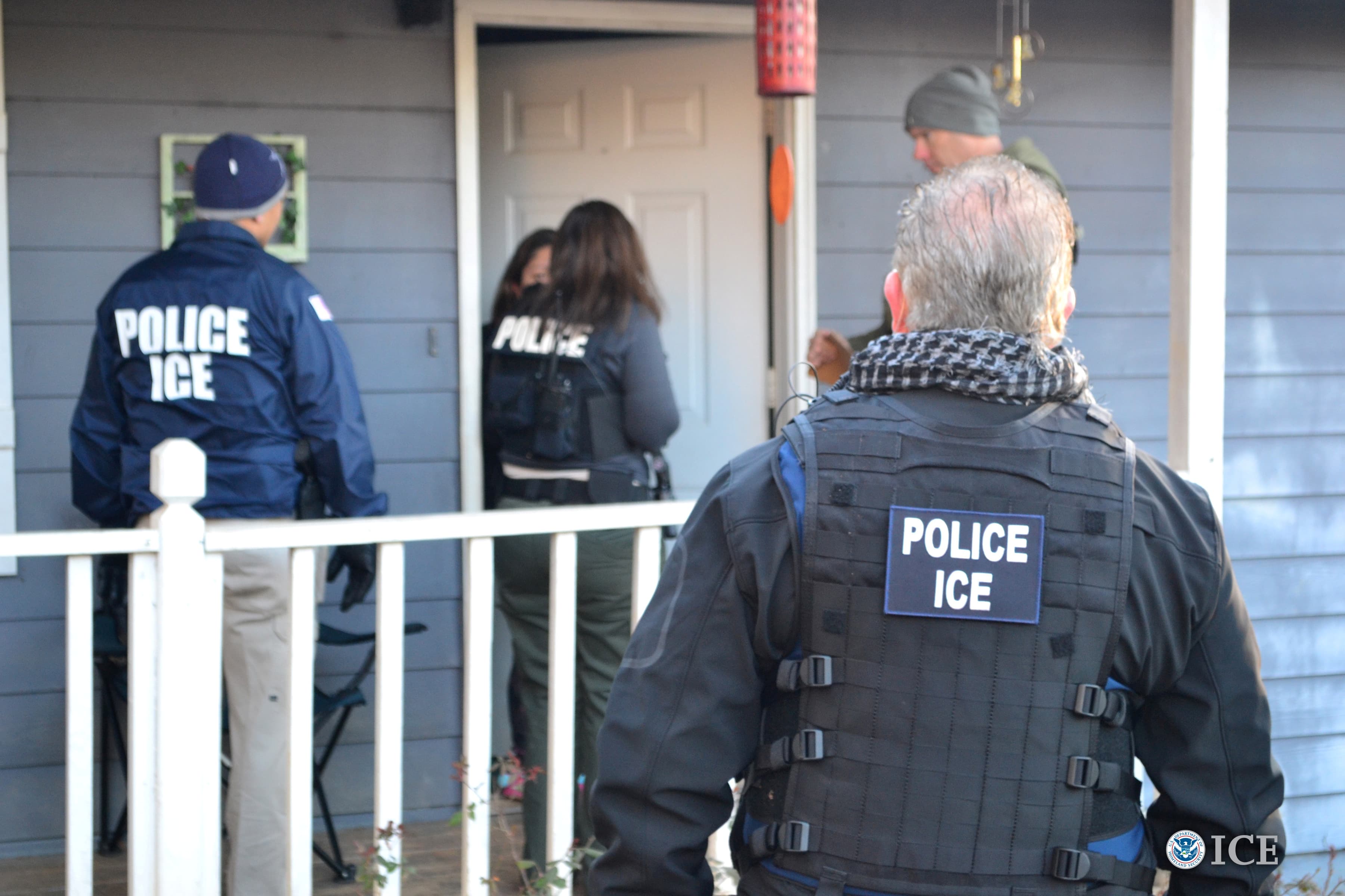 Men in uniform open the door to a house.