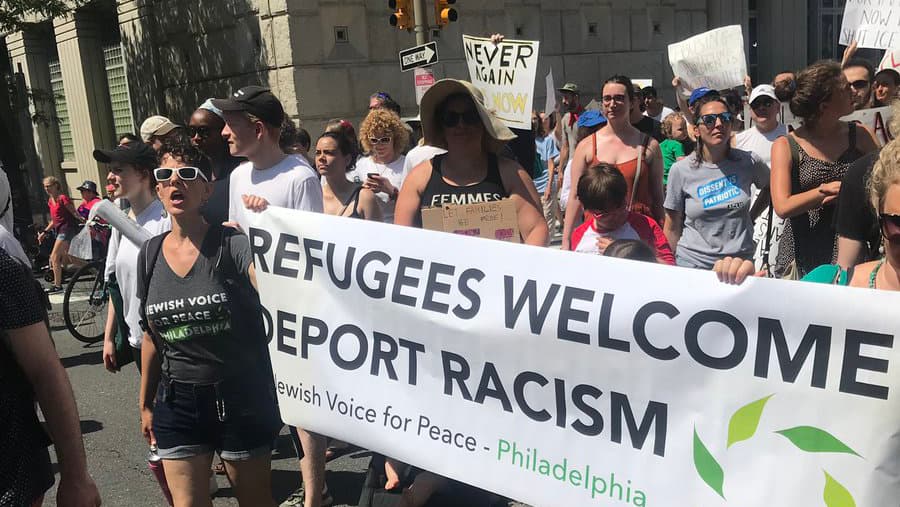 A group of protesters walk down a street holding a sign