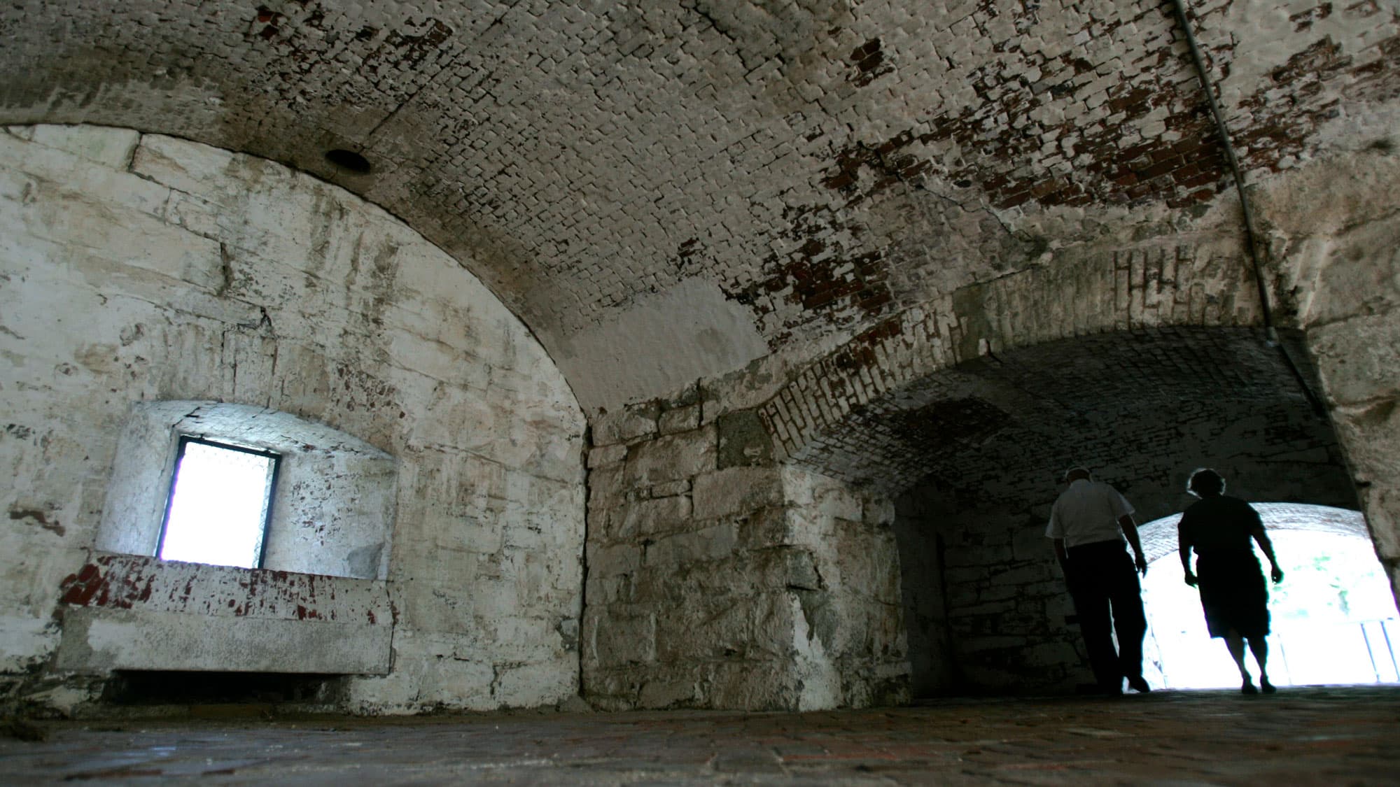 A couple is backlit against a stark stone fort interior.