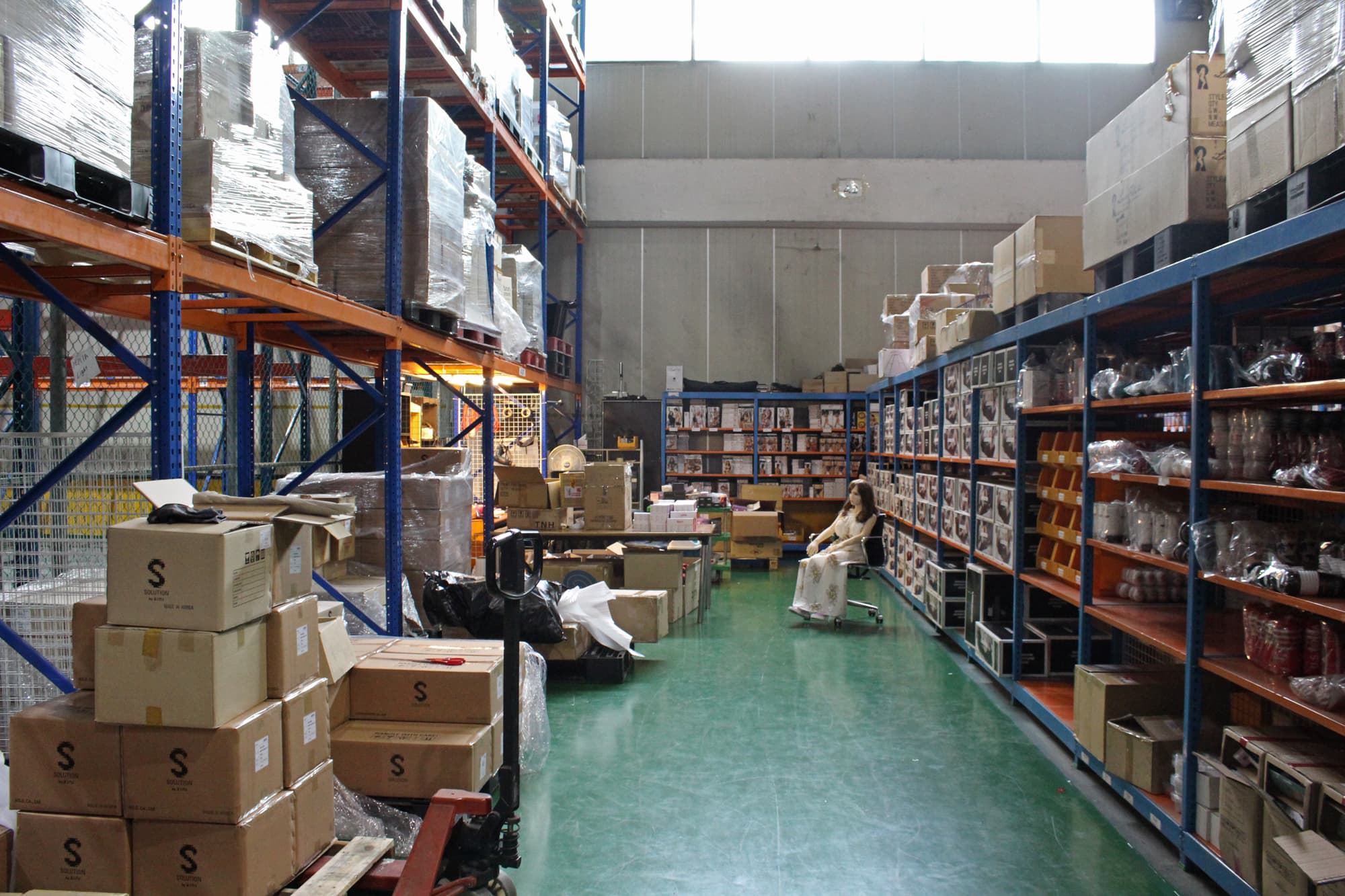 A plastic sex dolls sits in an office chair in a warehouse