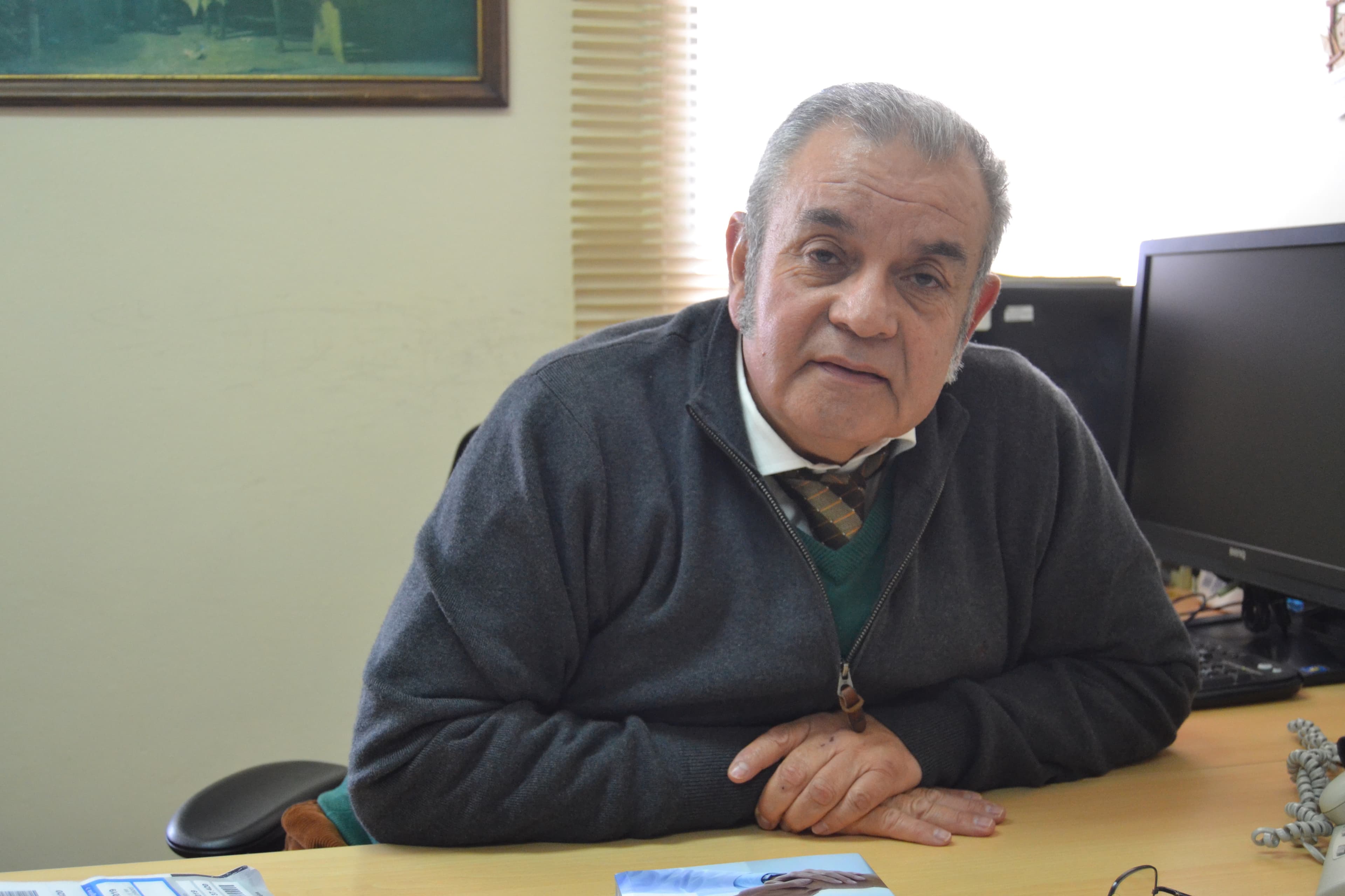 A man sits with his arms crossed at a desk.