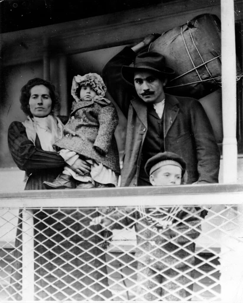 Immigrant family on a ship. Man holds their bundle of possessions on his back.