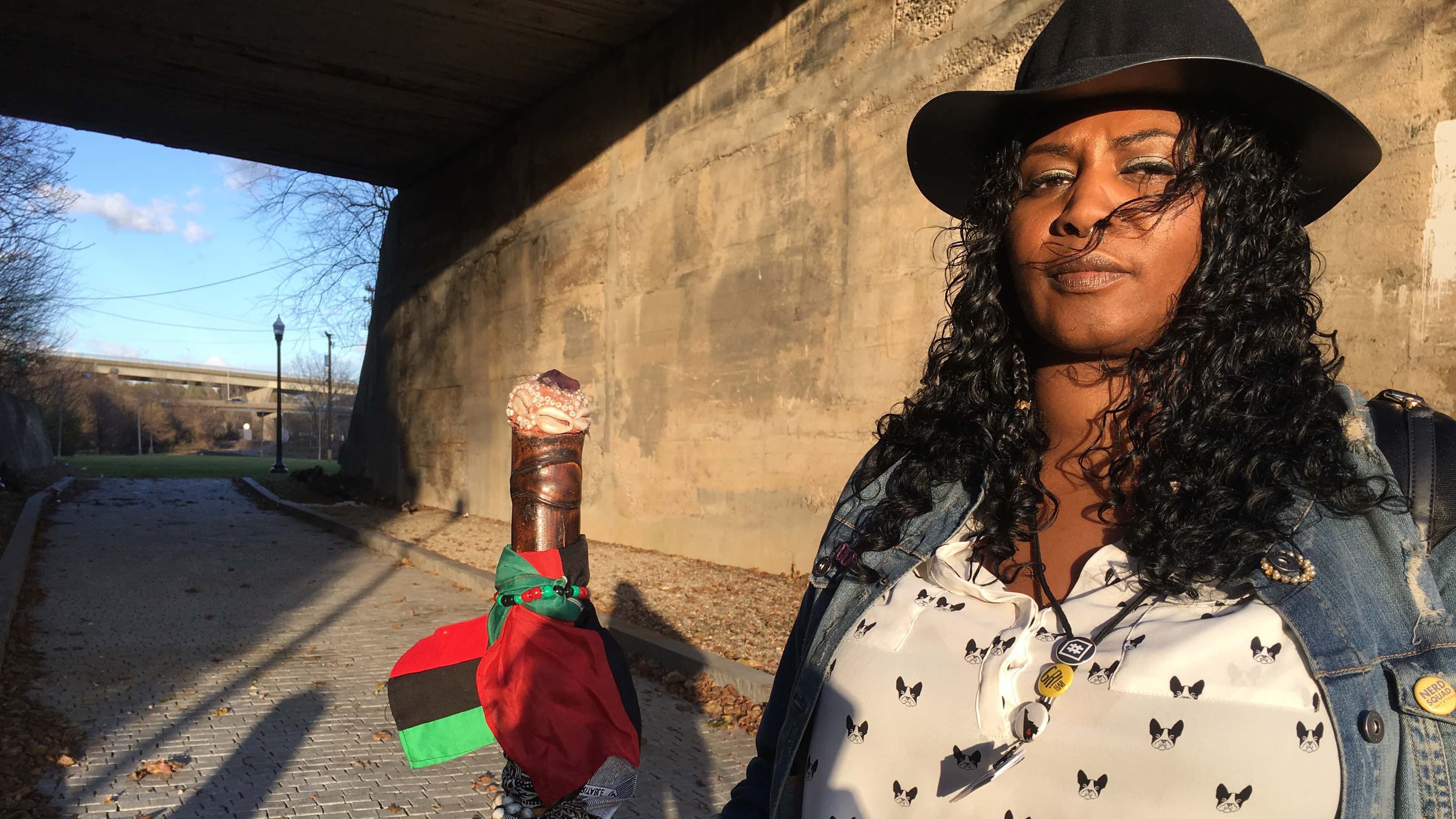 A black woman stands with a staff.