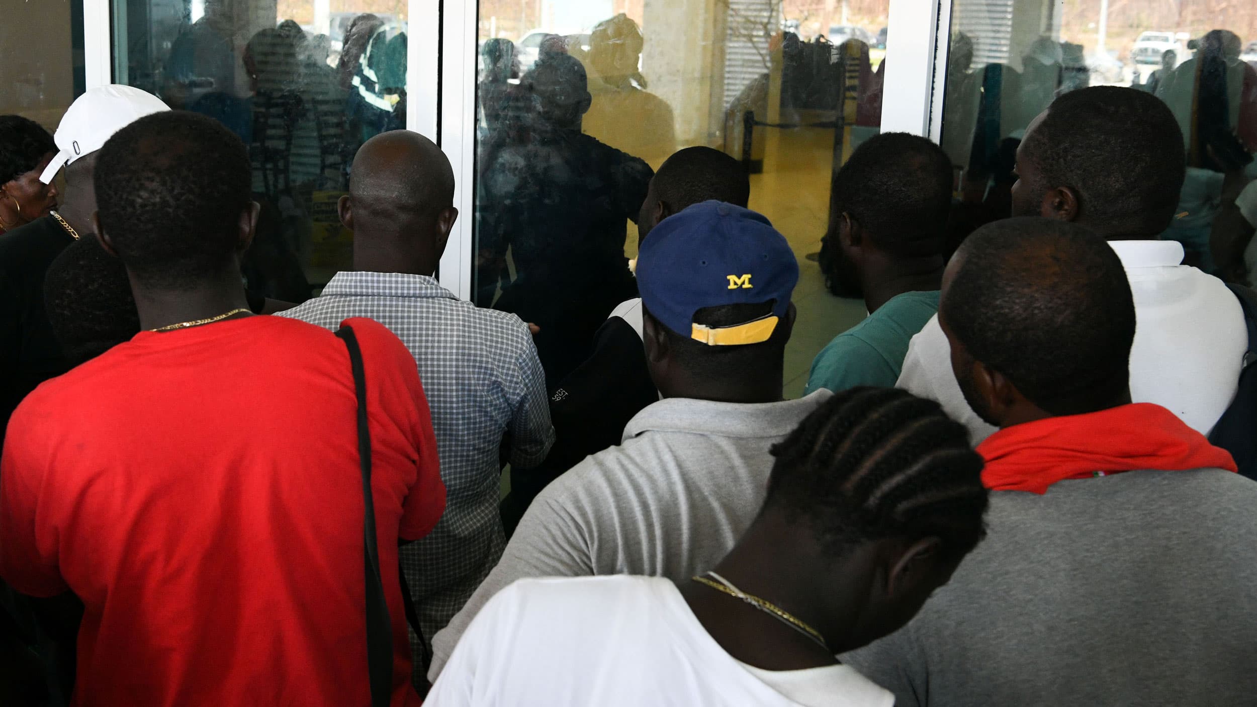 People huddle outside glass doors in a big group