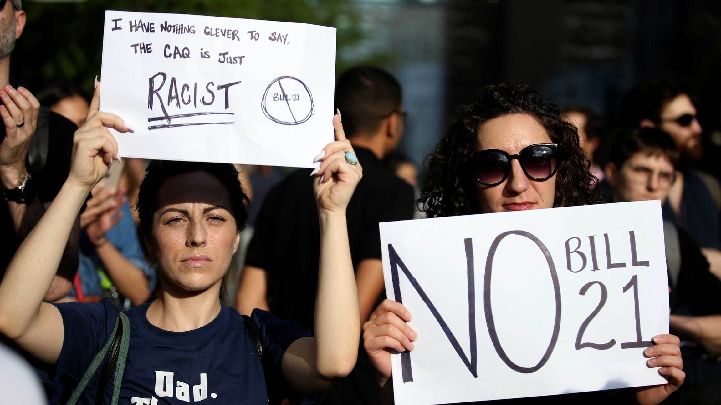 Two women hold protest signs that say No bill 21