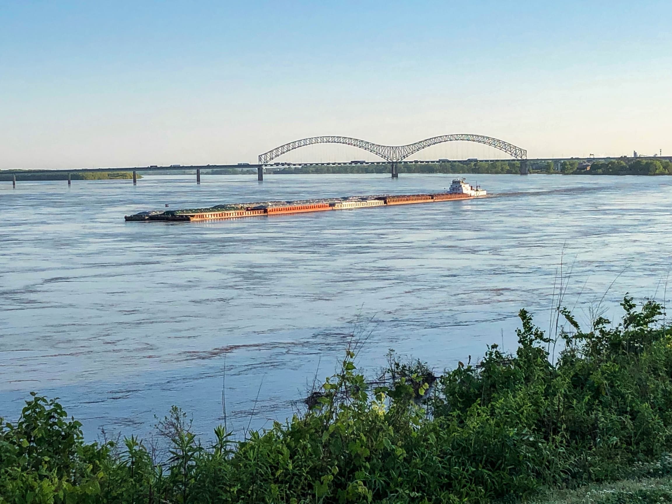 A barge is shown in the distance traveling on a blue river.