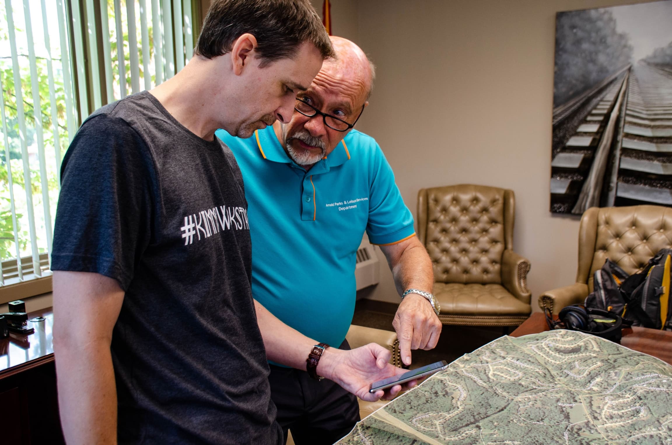 Two men are shown speaking to each other with one holding a mobile phone.