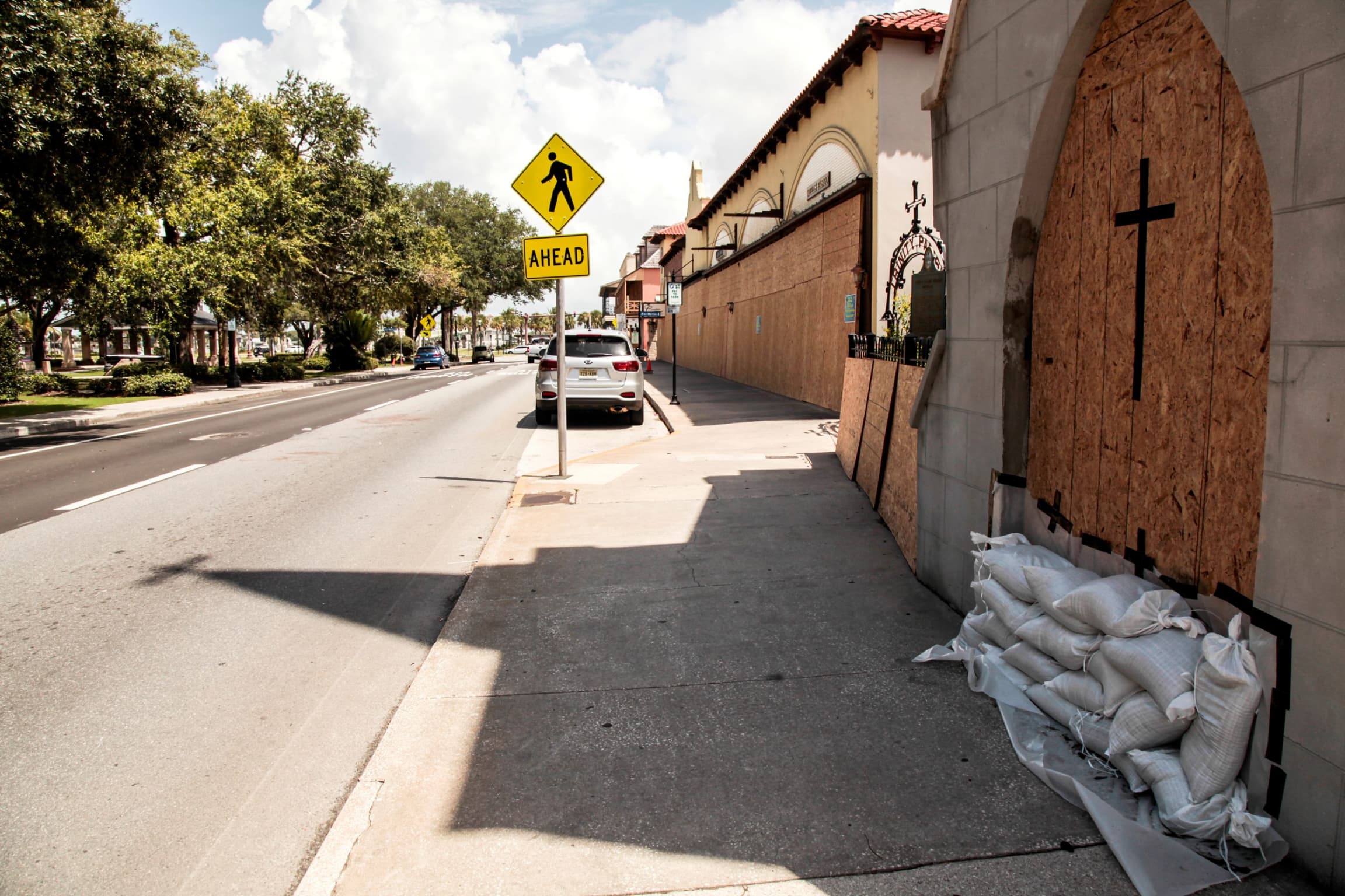A church is shown with its windows boarded up with several sand bags lining the base of the doorway.