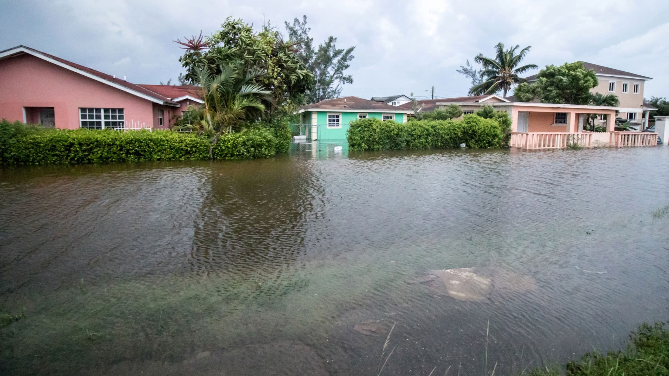 A row of houses are shown from across a flooded street with water up to the front porch of one of the houses.