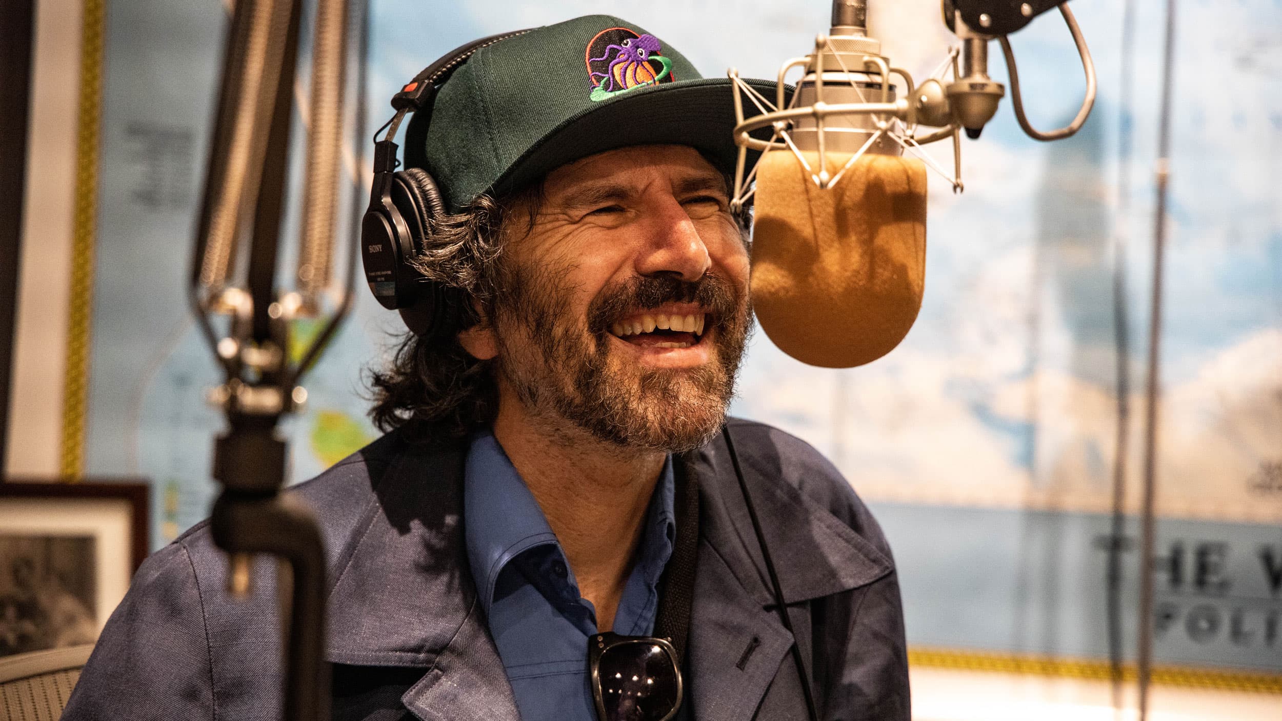 A white man in a hat laughs into a radio mic