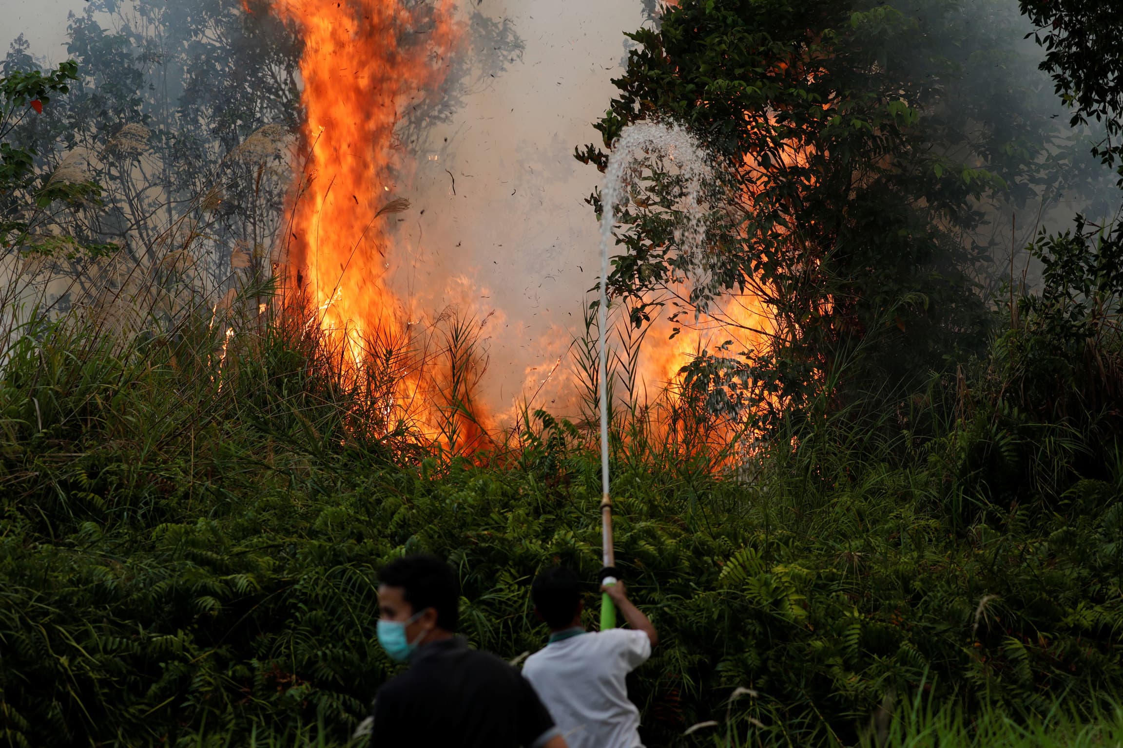 A man is shown holding a large hose and shooting water at a blazing fire.