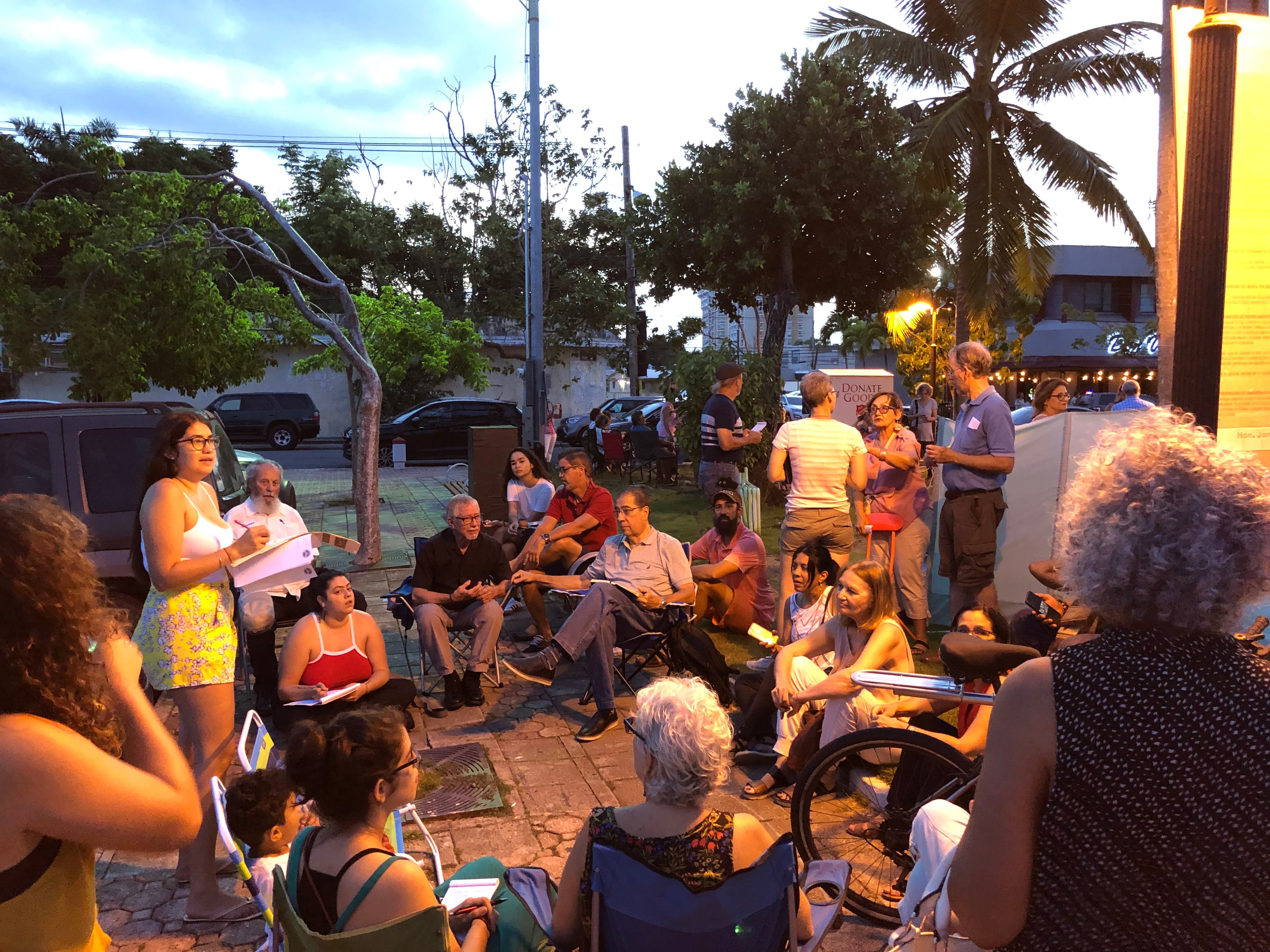 A group of people sit in a circle on a porch at dusk