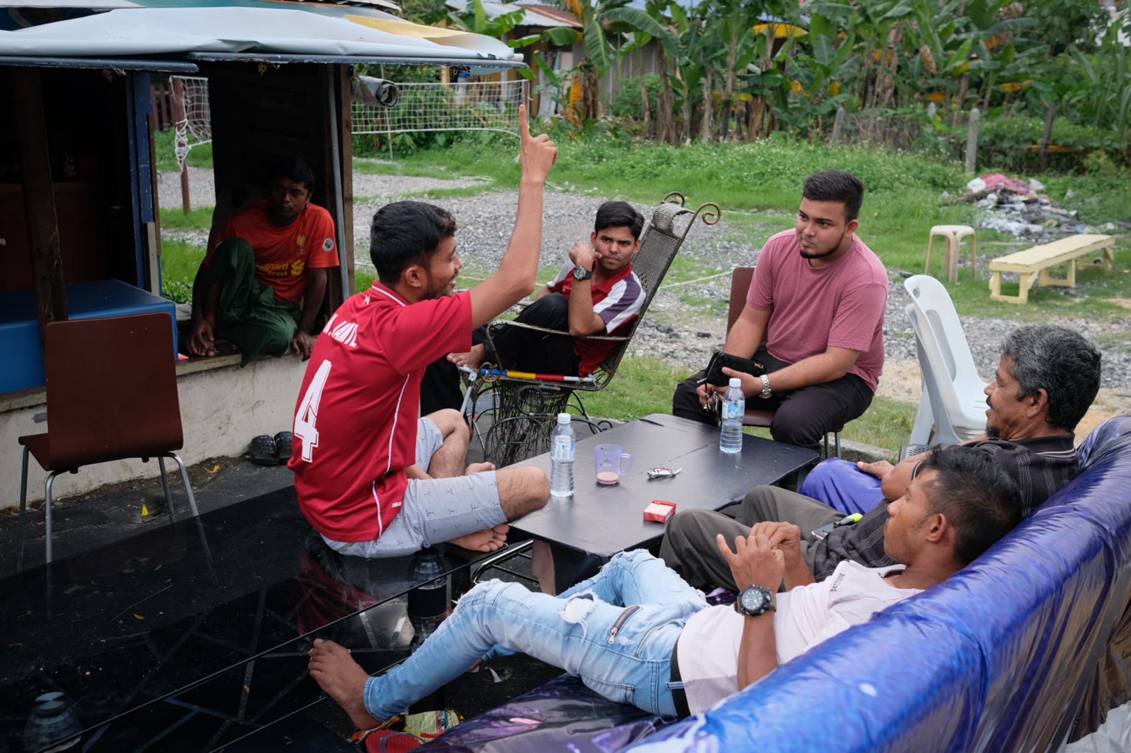 Young men sit around black tables in makeshift living room setting.
