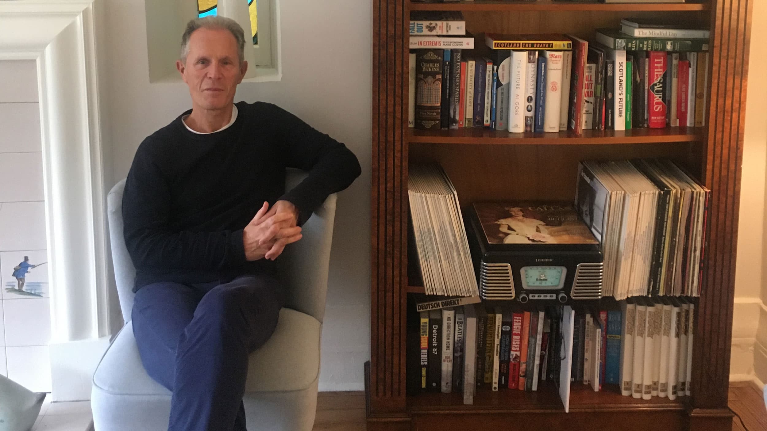 A portrait of Blair Jenkins sitting in his stair next to a book case
