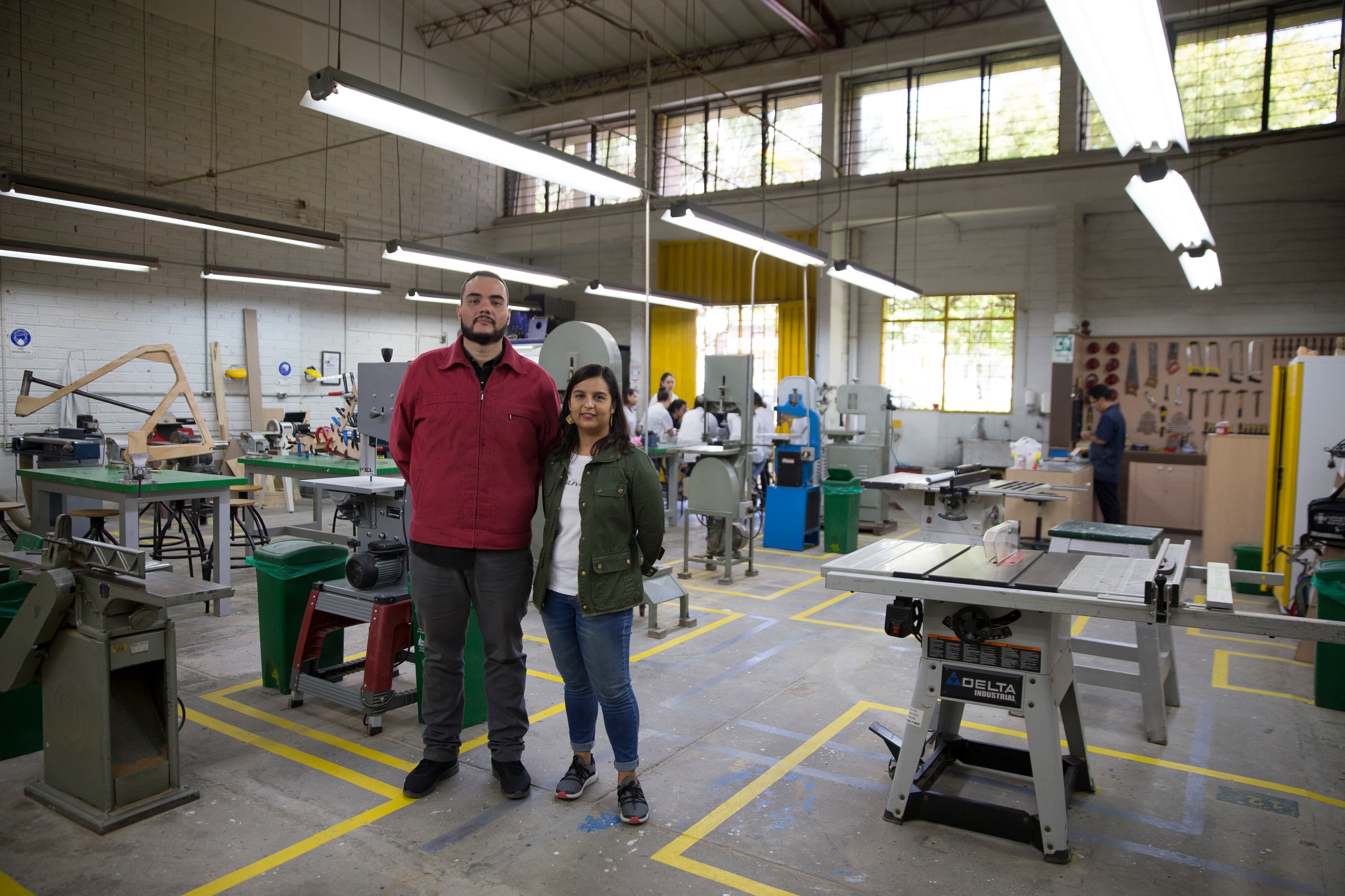 Two scientists stand in their lab near work tables with low-hung florescent lights