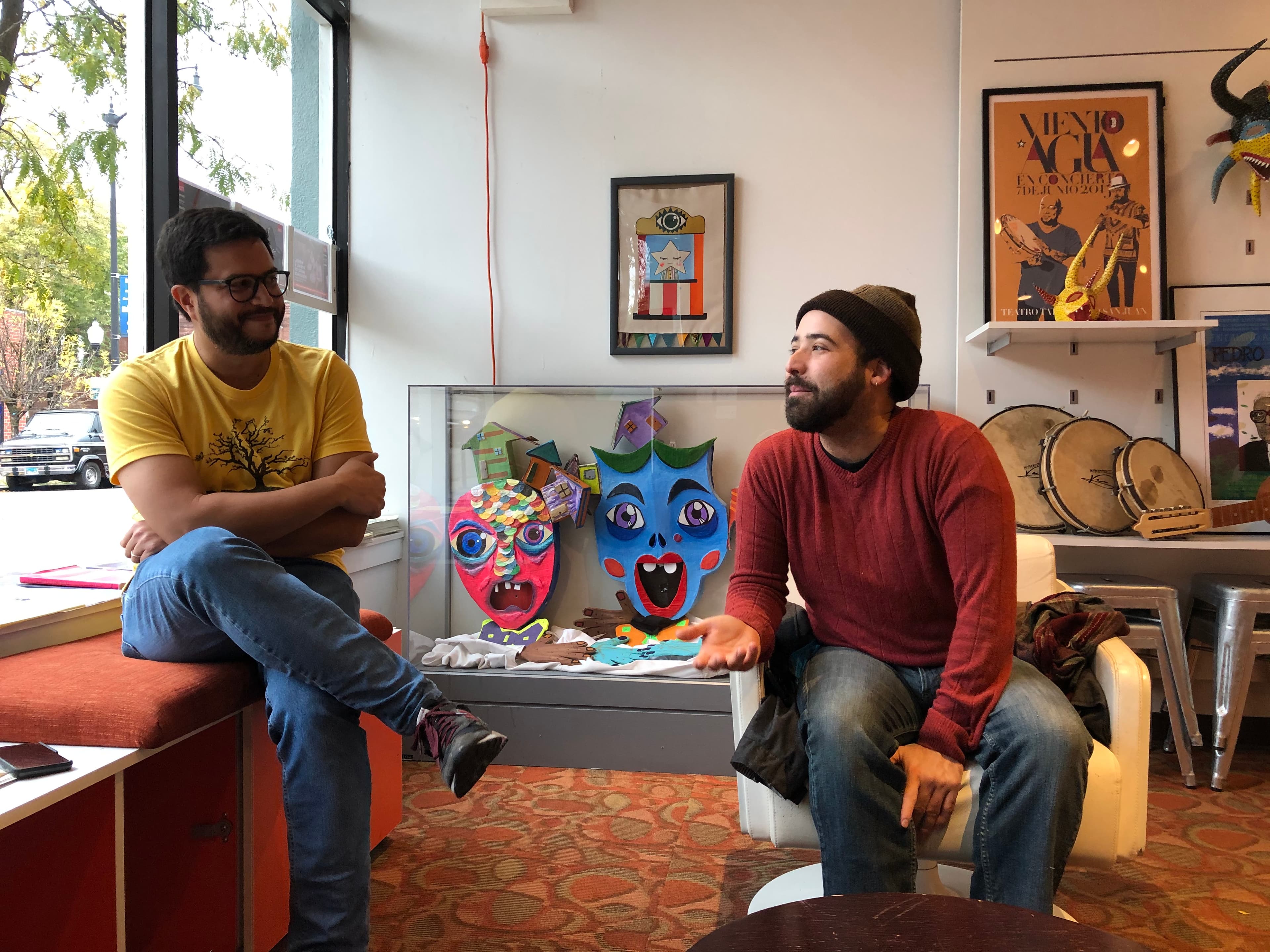 Two men sit in a sun-lit lobby with books and plants.