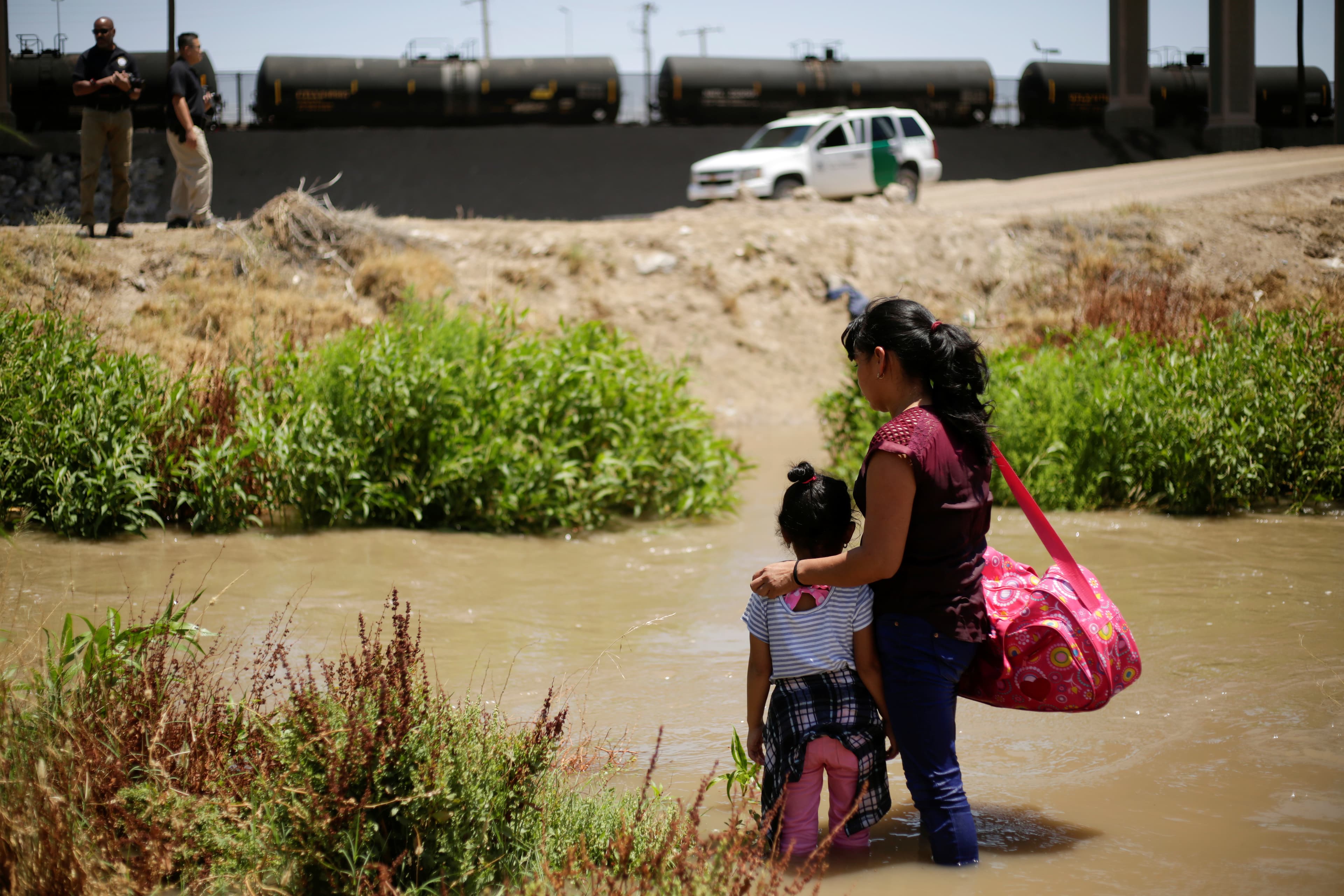 A woman and a young girl stand together on the banks of a river.