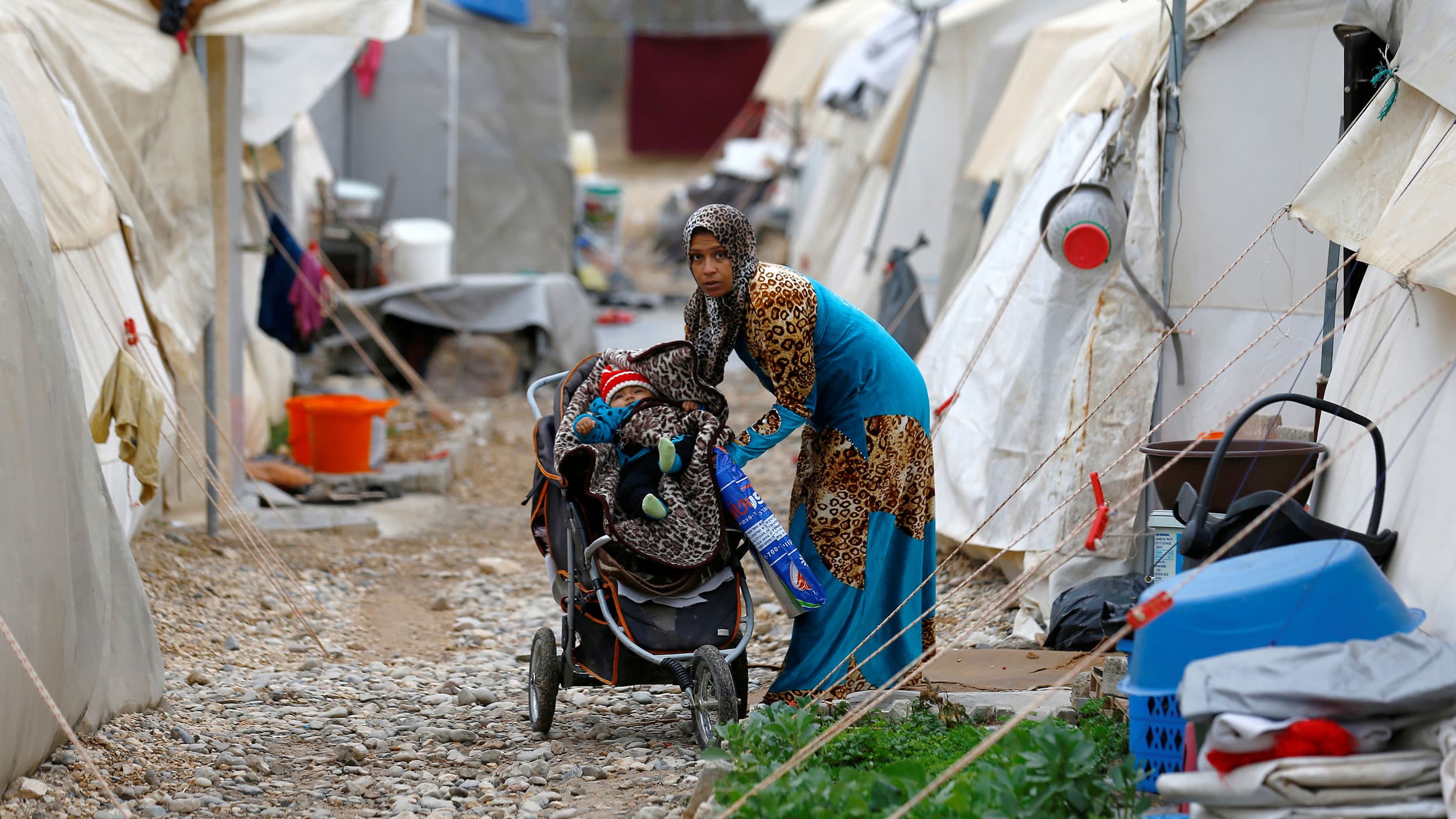 A woman in a headscarf looks at the camera as she puts a baby in a stroller