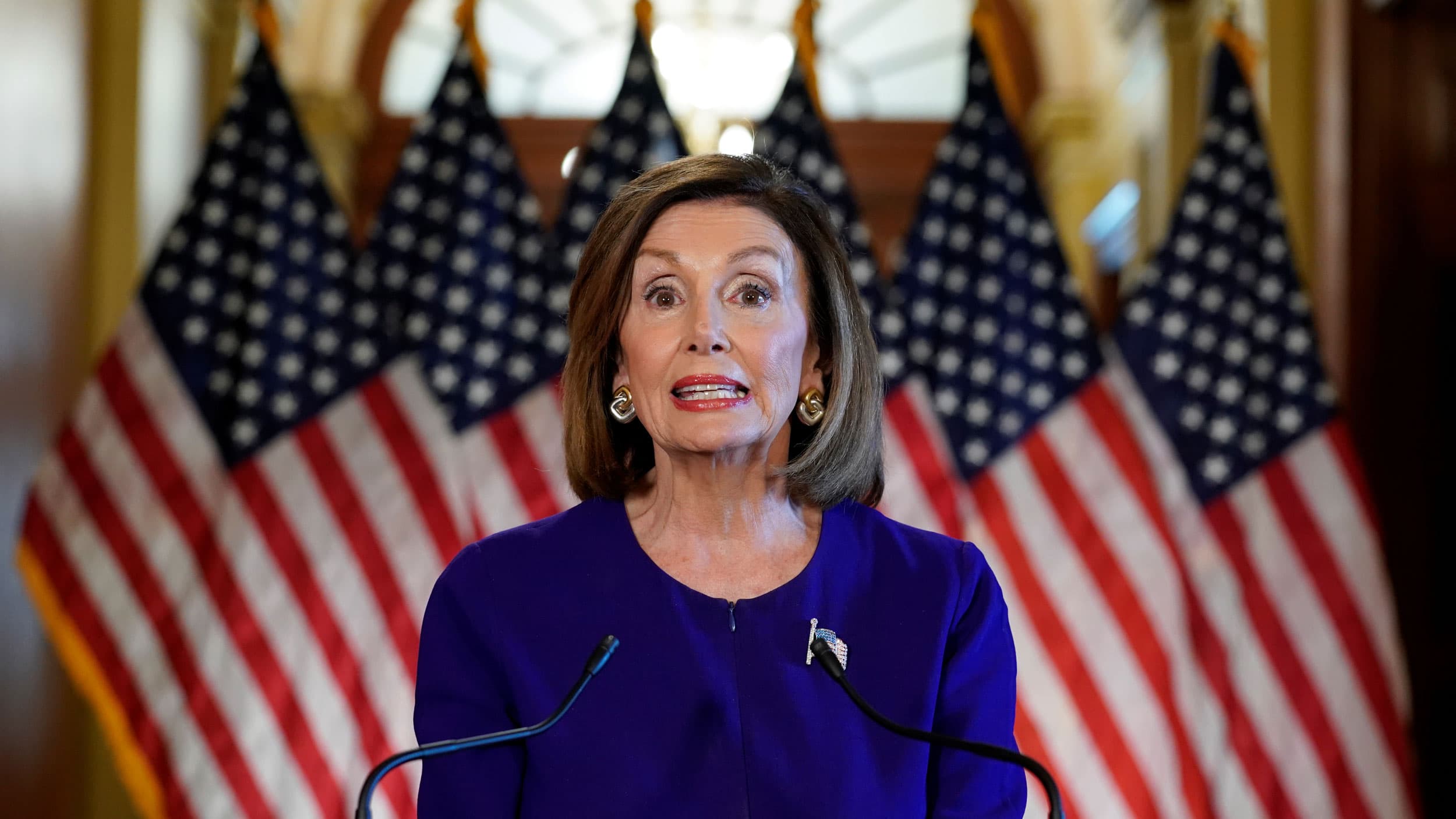 Nancy Pelosi in blue in front of American flags
